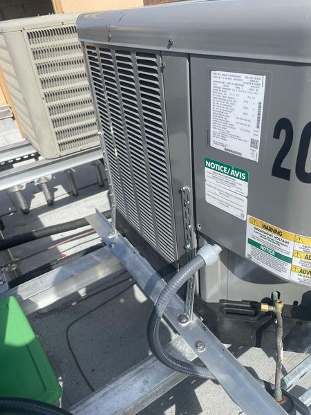 Outdoor air conditioning unit on a rooftop, with metal grating and electrical conduit.