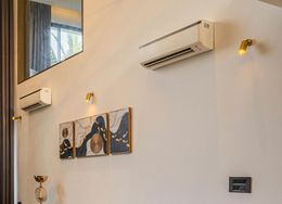 White wall with two AC units, three paintings, and wall sconces.