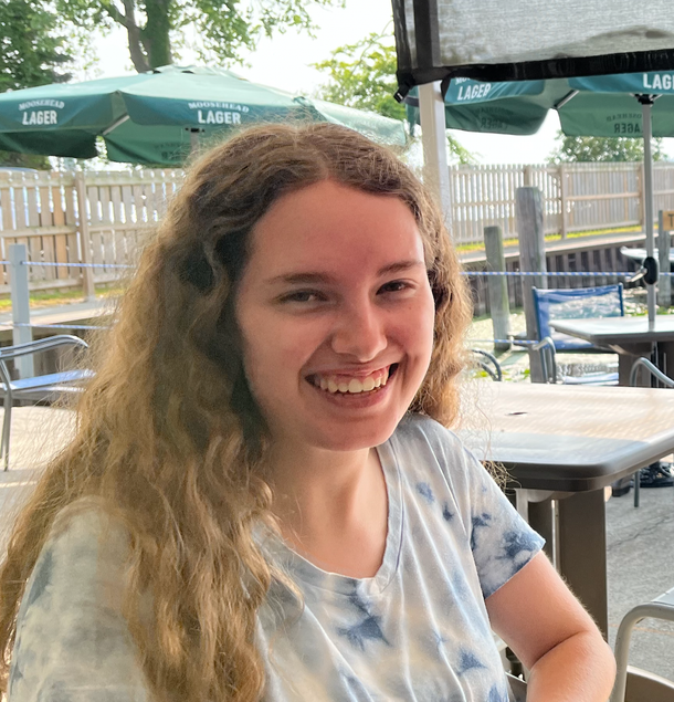 A young lady is smiling while sitting at a table with green umbrellas in the background