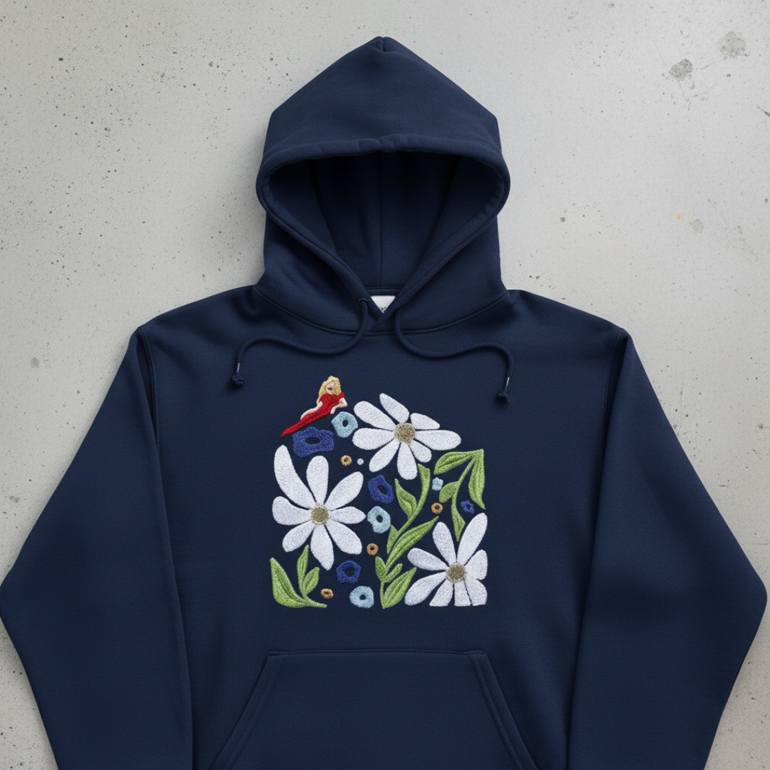Navy hoodie with floral embroidery: white daisies, blue flowers, green leaves, and a small red bird.