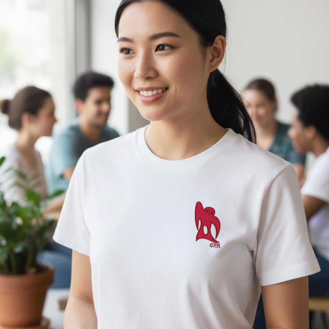 Woman in white t-shirt smiles, a red logo on shirt. Group of people in background.