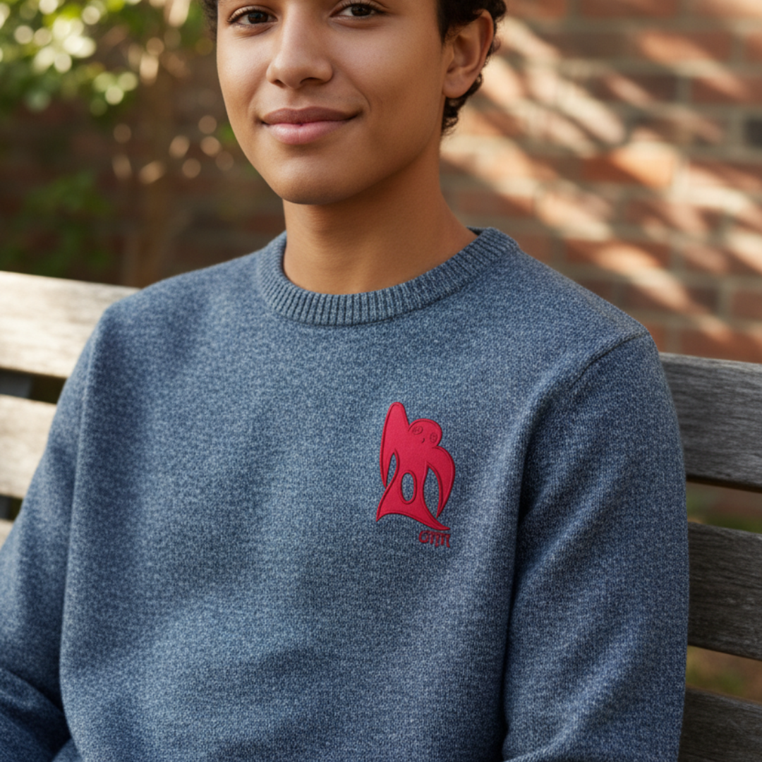 Person wearing a blue sweater with a red embroidered design on a wooden bench, smiling.
