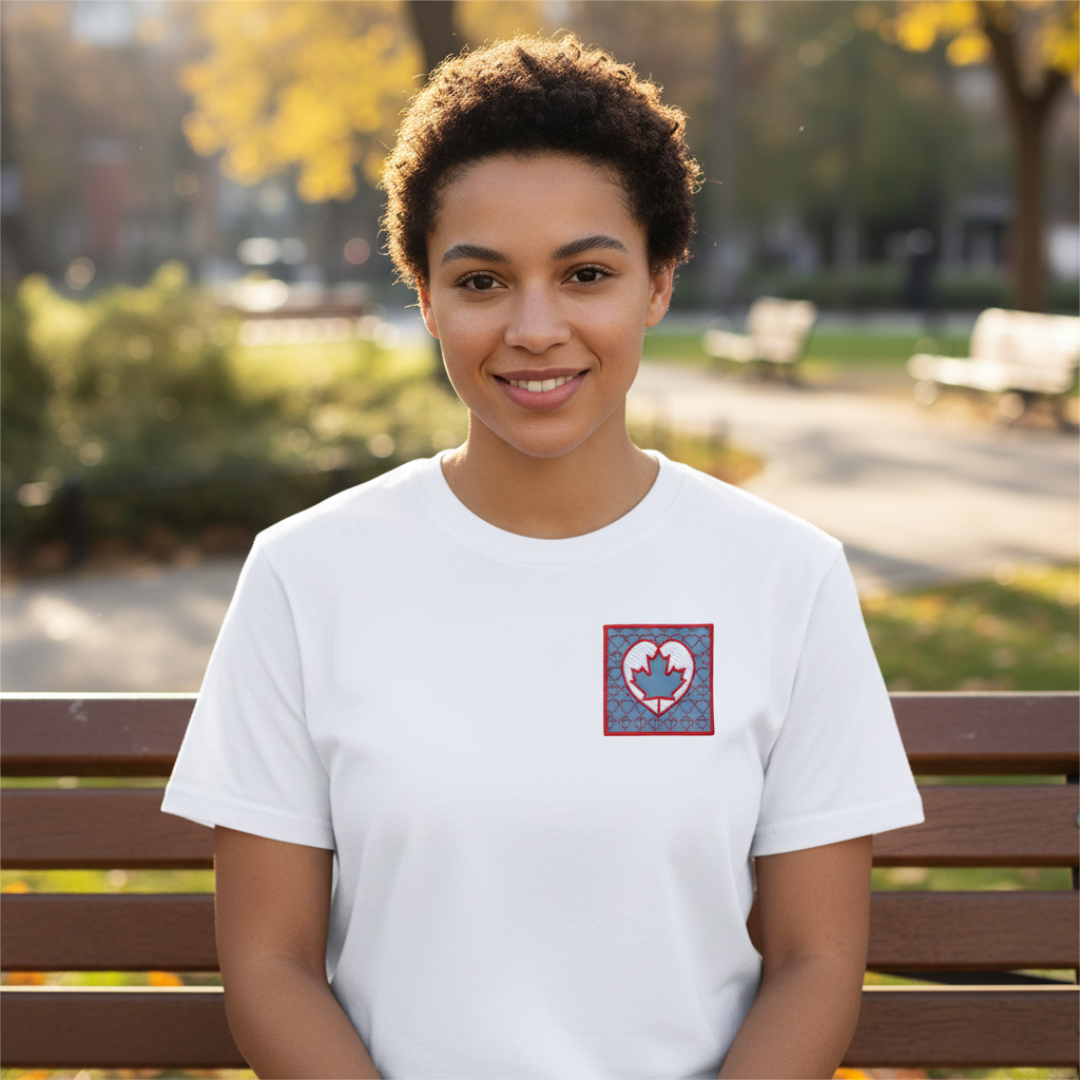 Woman in white shirt with heart and maple leaf design, sitting outdoors smiling.
