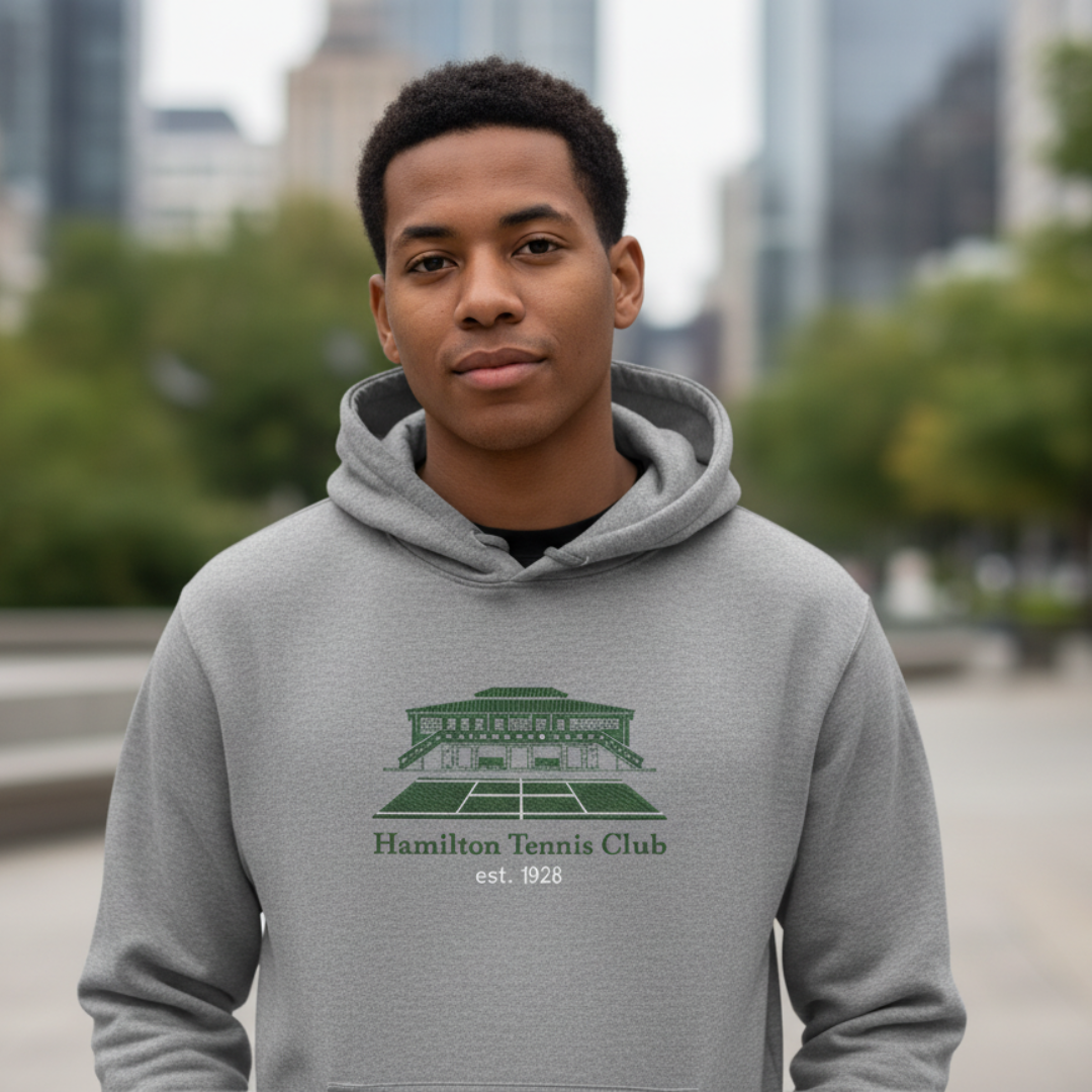 Man wearing gray hoodie with green Hamilton Tennis Club logo, standing outdoors.