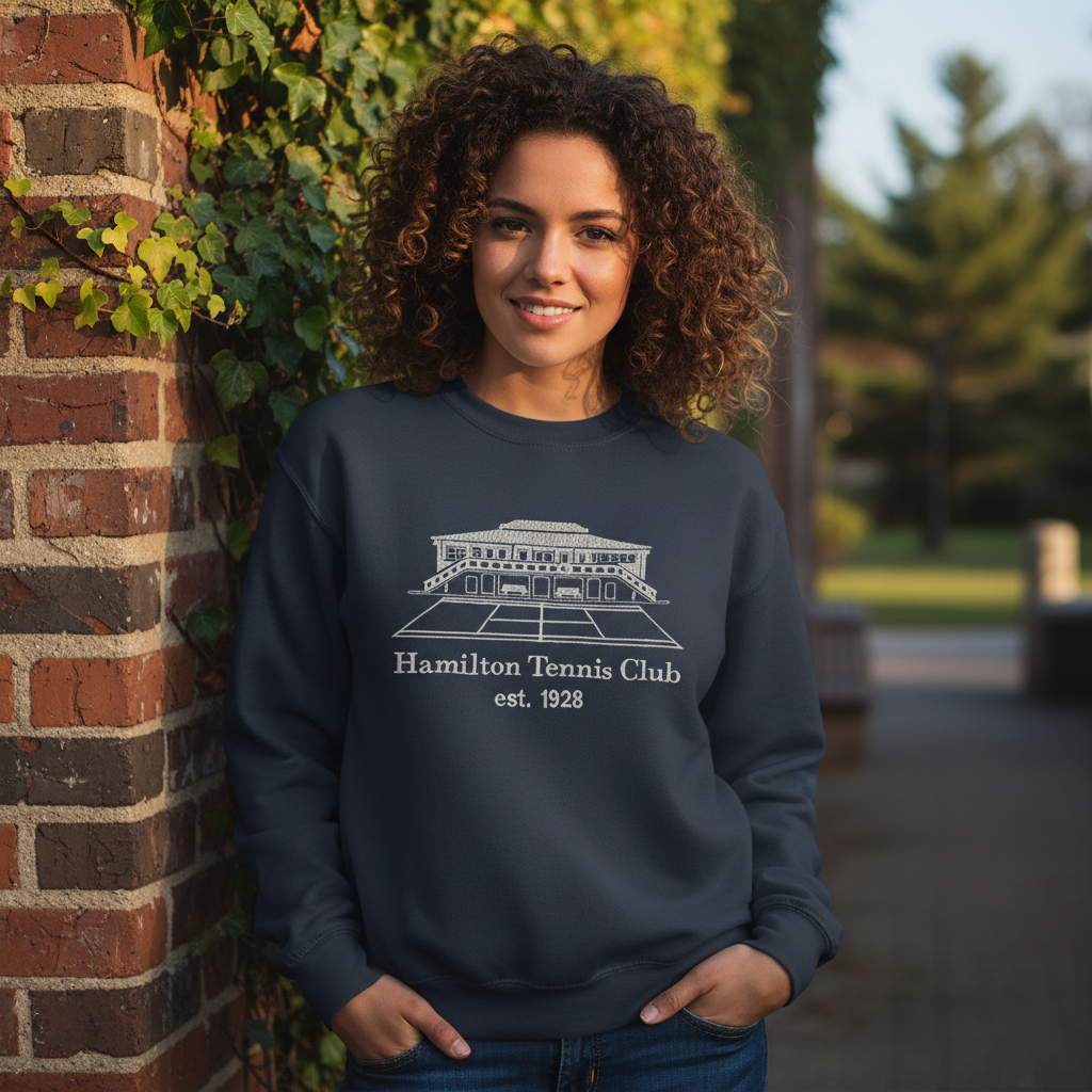 Woman wearing a navy sweatshirt with a white Hamilton Tennis Club logo, standing outdoors.