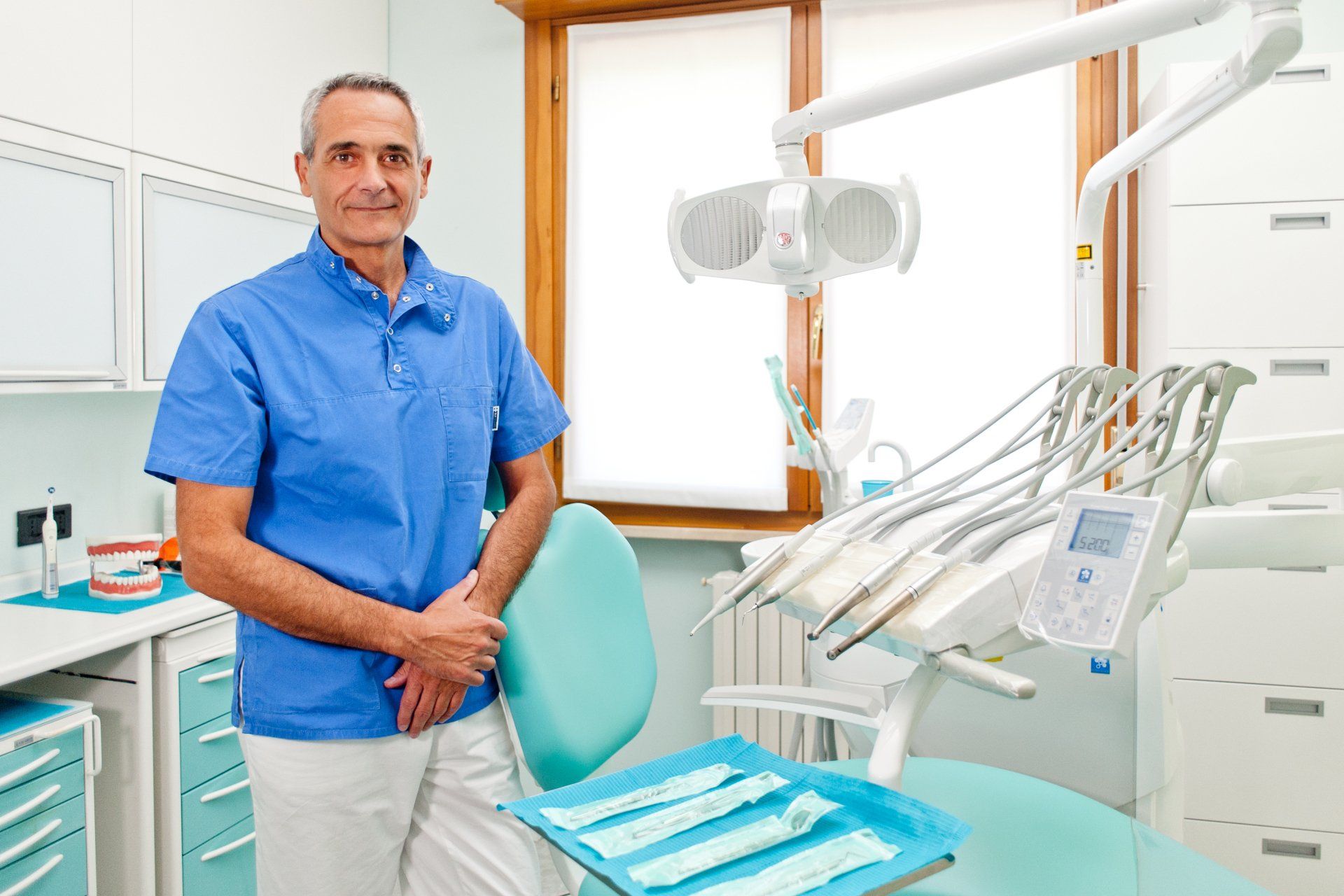 Un dentista è in piedi in uno studio dentistico accanto a una poltrona odontoiatrica.