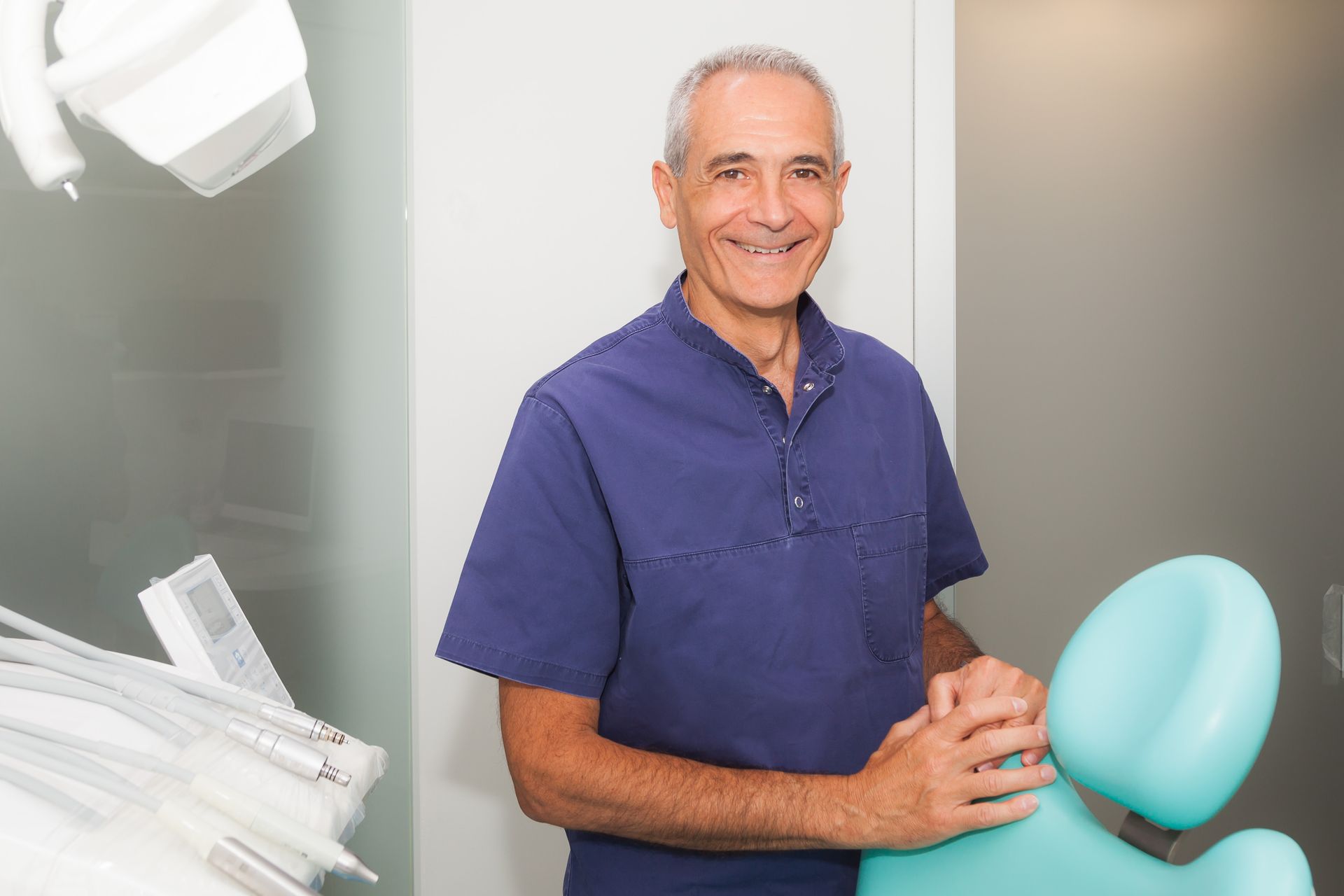 Un dentista è in piedi in uno studio dentistico accanto a una poltrona odontoiatrica.