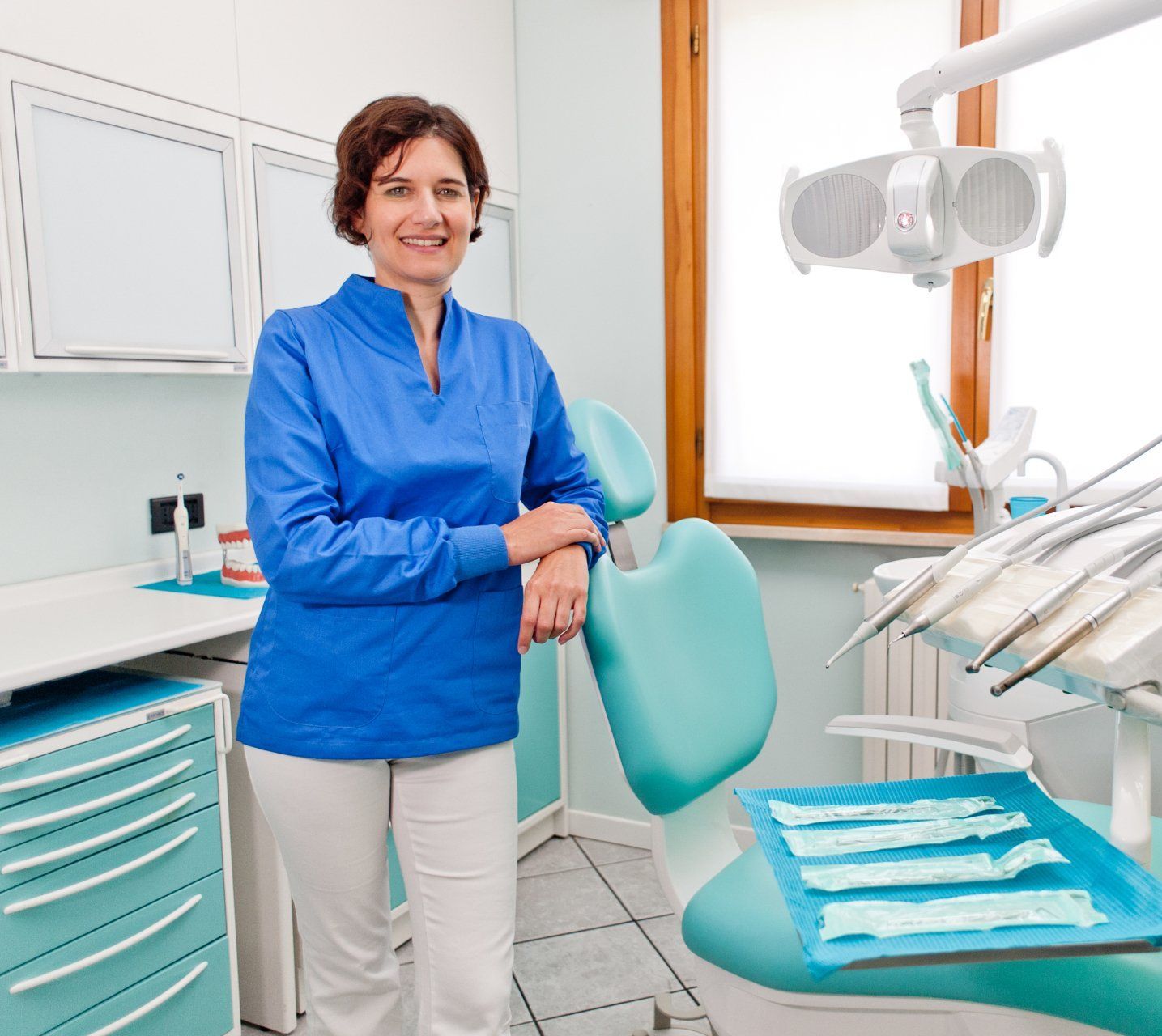 Una donna è in piedi accanto alla poltrona del dentista in uno studio dentistico.