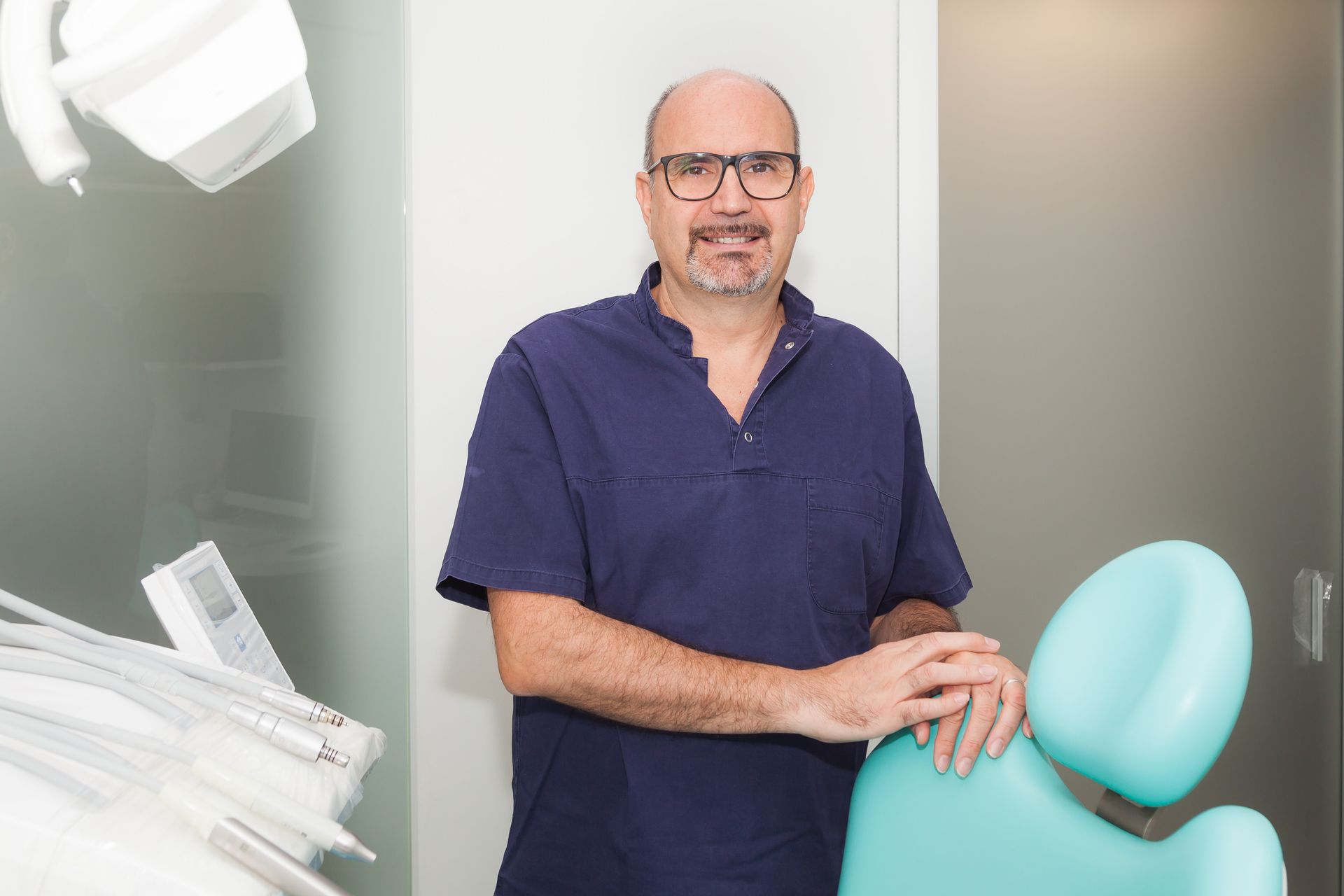 Un dentista è in piedi in uno studio dentistico accanto a una poltrona odontoiatrica.