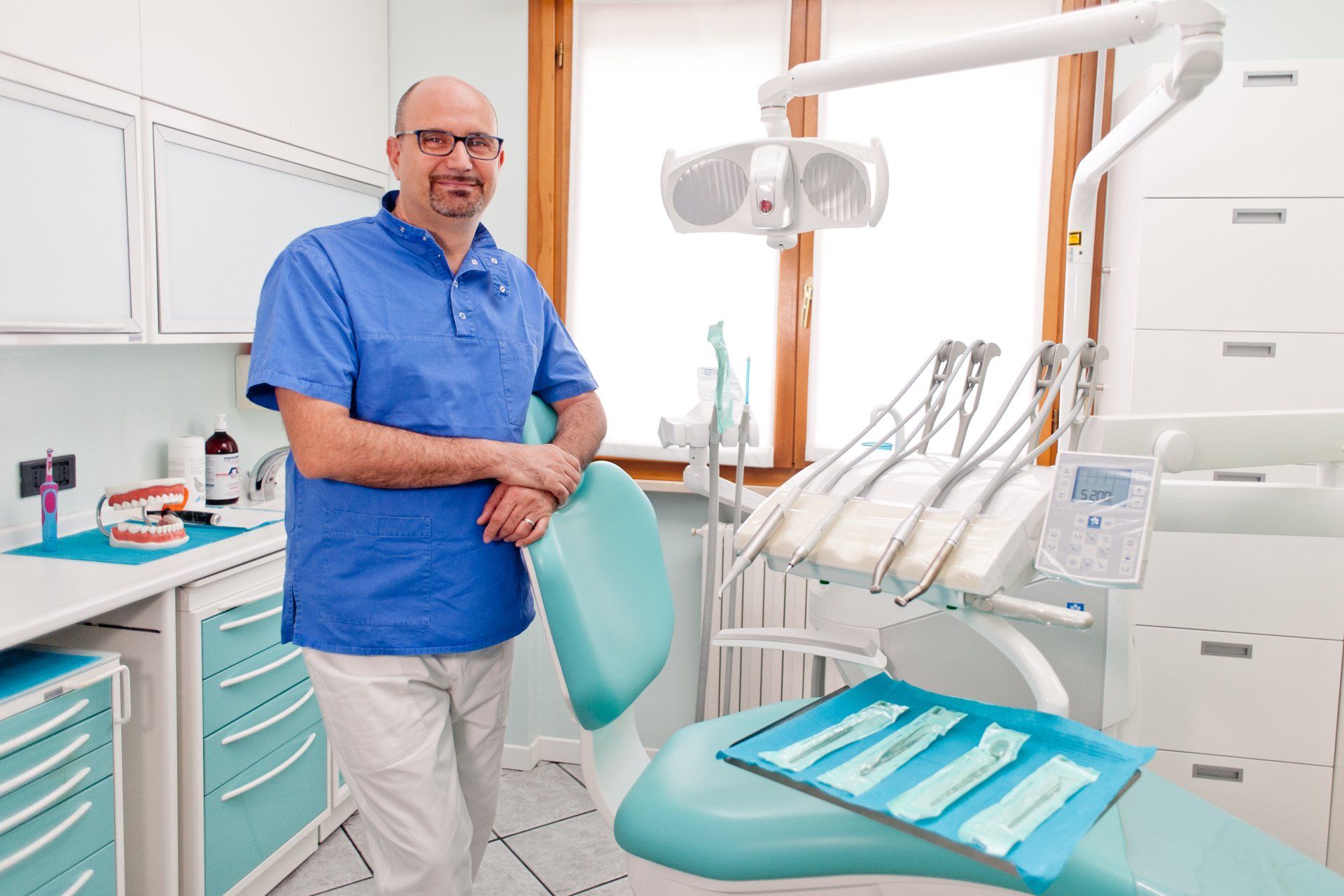 Un dentista è in piedi in uno studio dentistico accanto a una poltrona odontoiatrica.