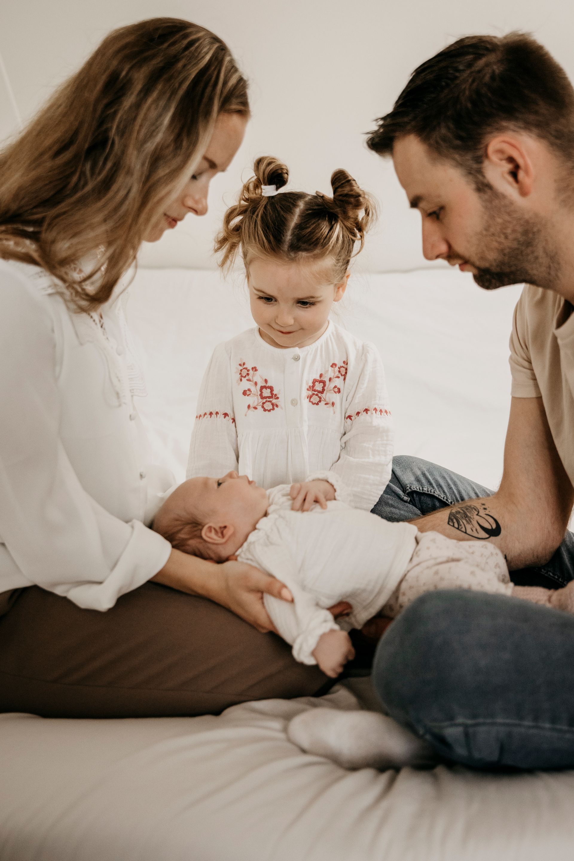 Een gezin zit op een bed met een pasgeboren baby en een klein meisje.