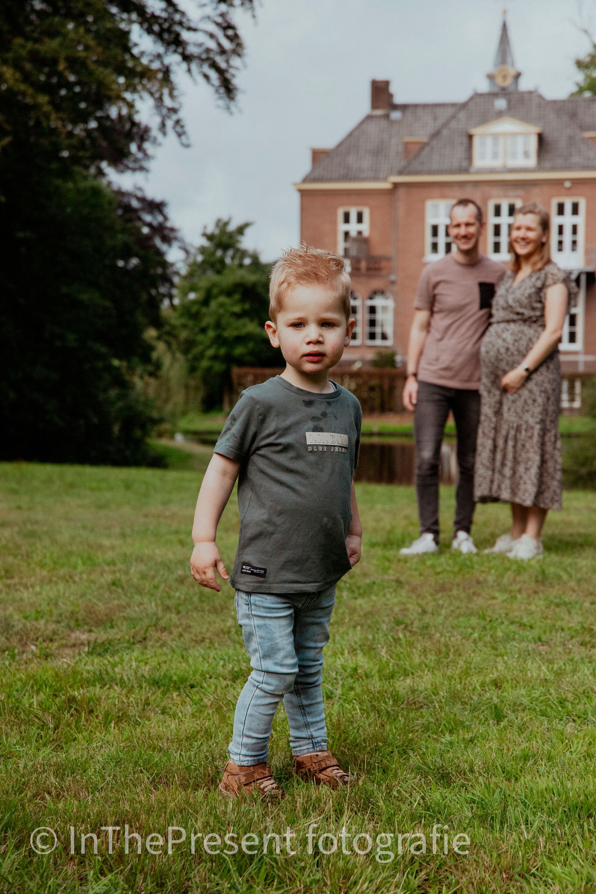 Een jongetje staat in het gras voor een zwangere vrouw en een man.