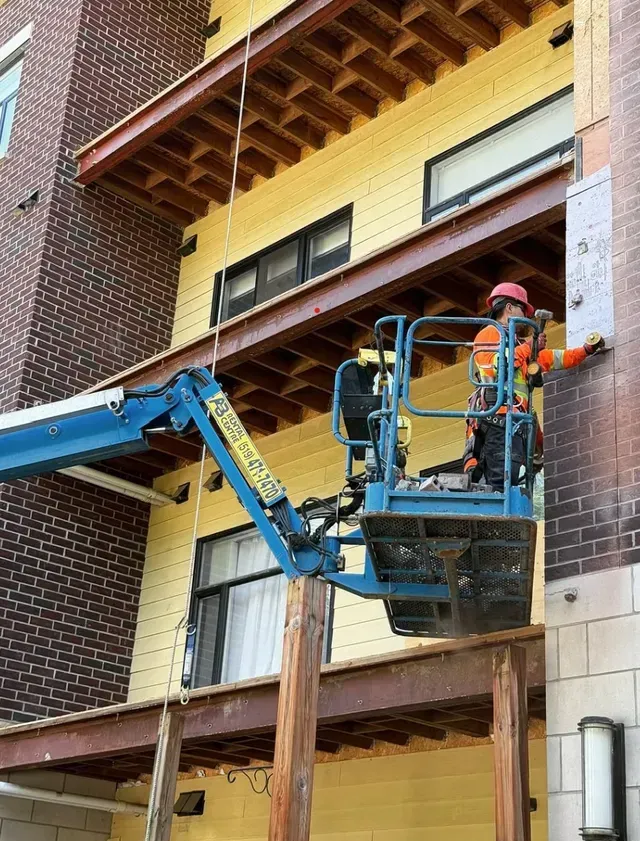 Worker in a blue lift repairing a brick building’s exterior wall.