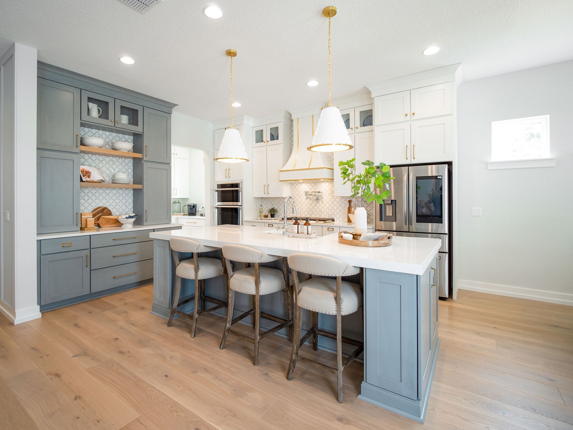 Bright white kitchen with blue cabinets, a large island, and hanging pendant lights over wood floors