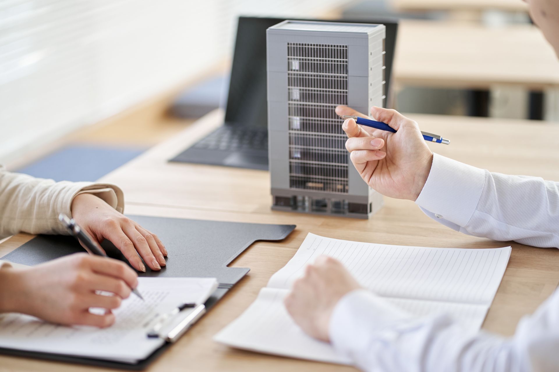 Hands working at a desk with a laptop, calculator, ruler, and blueprints for design planning