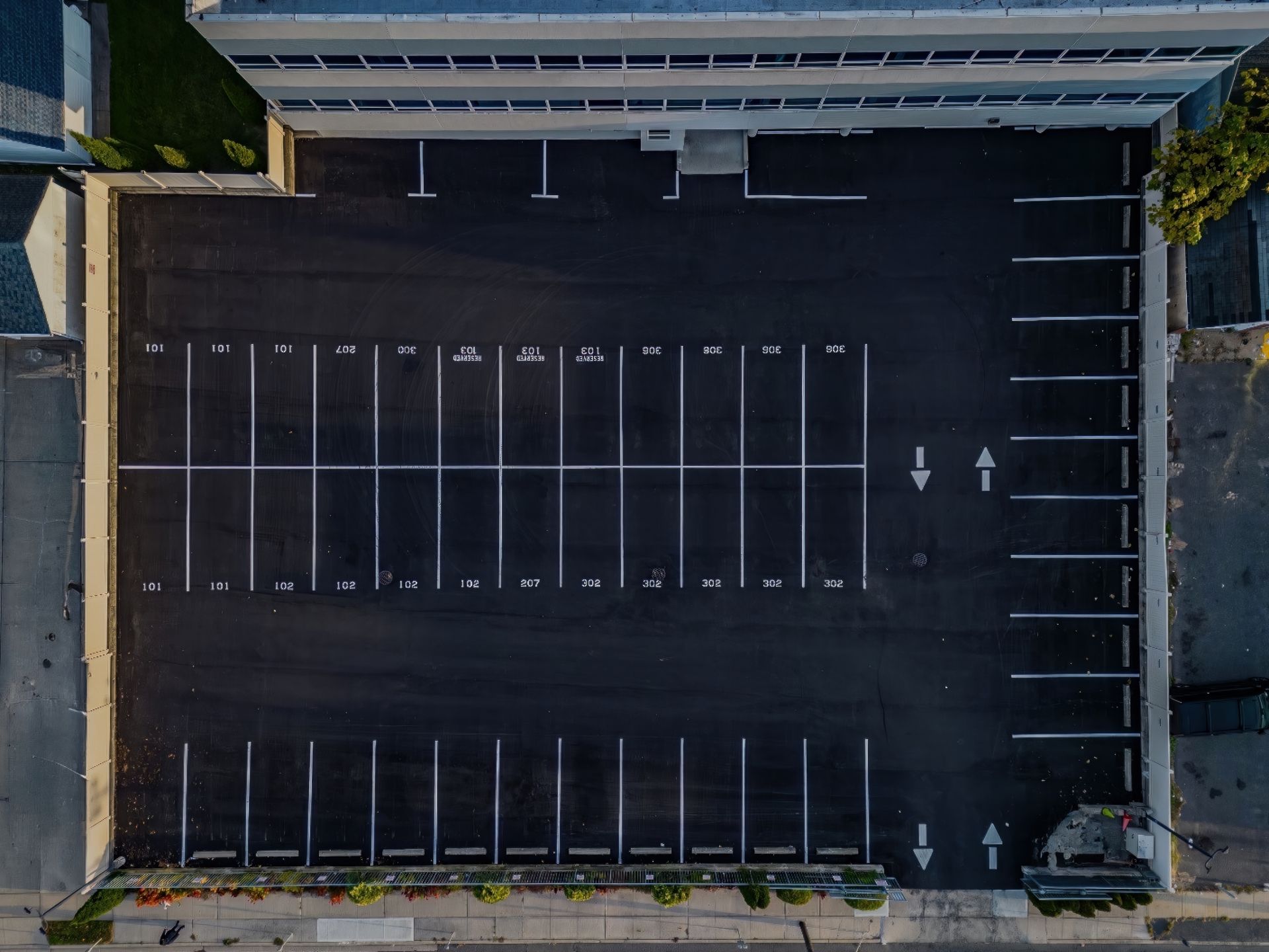 Empty aerial view of a blacktop parking lot beside a building, marked with white parking lines and arrows