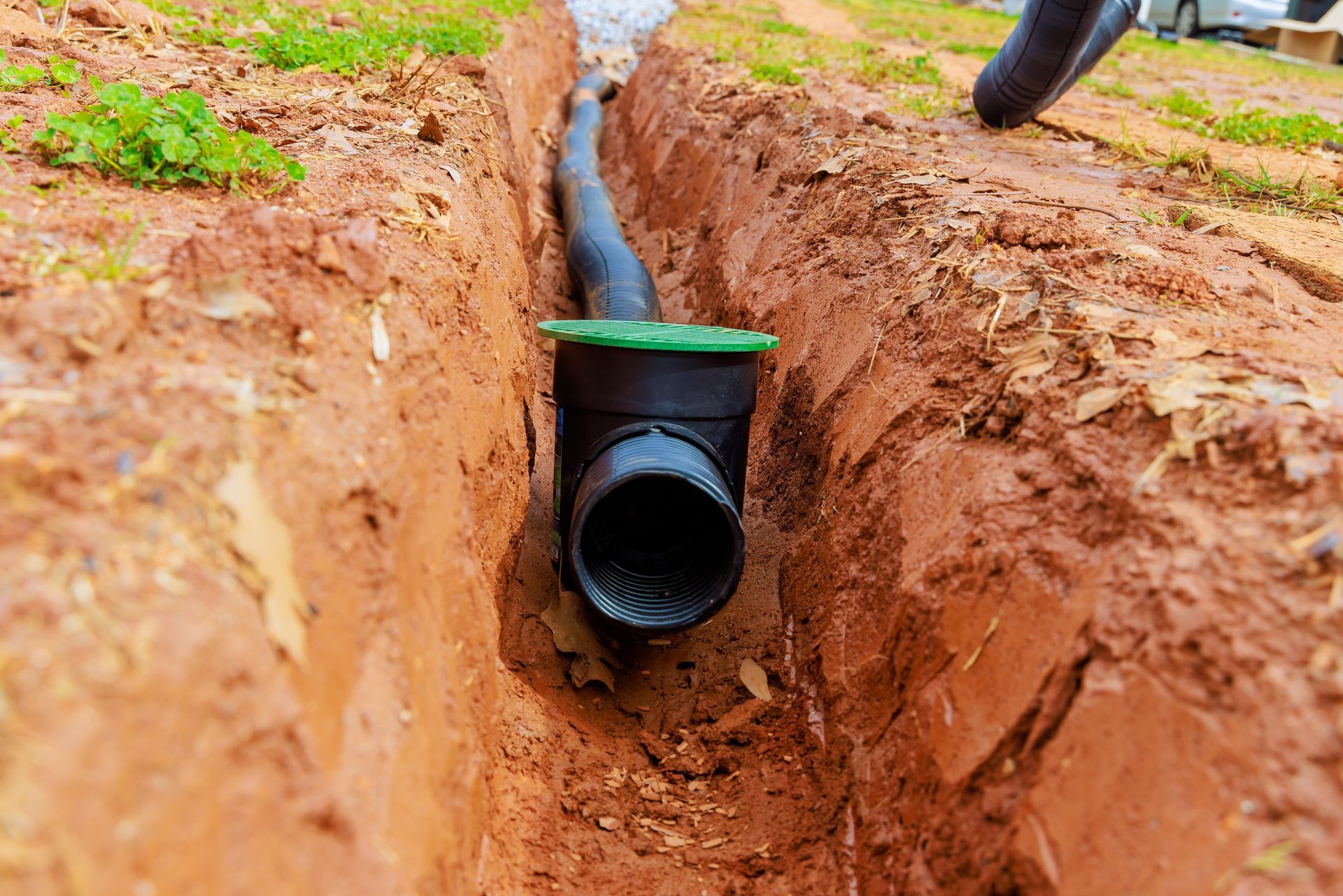 Black drainage pipe laid in a muddy trench with green collar and connected hose