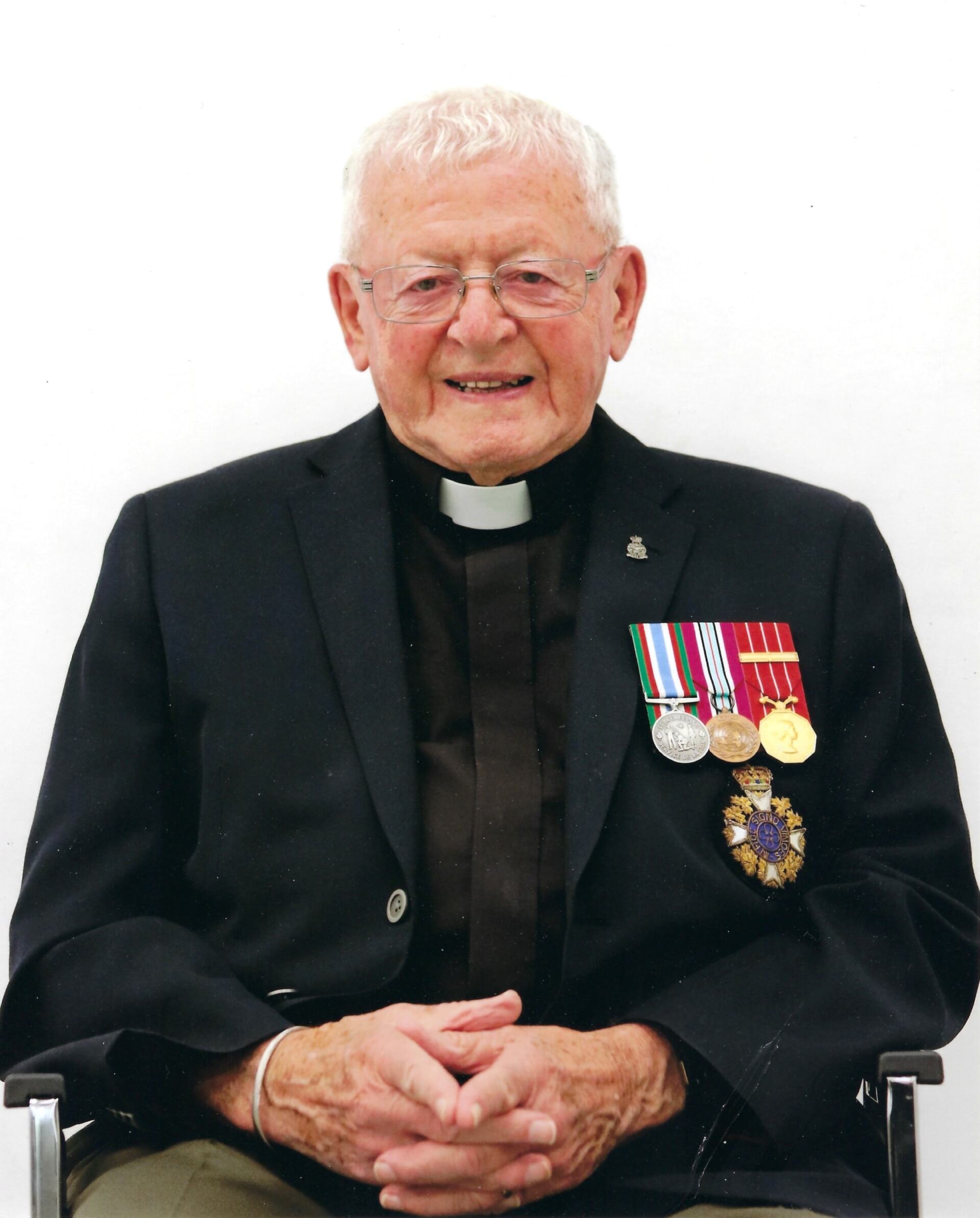 Portrait of Rev. Bob Jones, wearing a liturgical collar a black suit with three metals on his lapel.