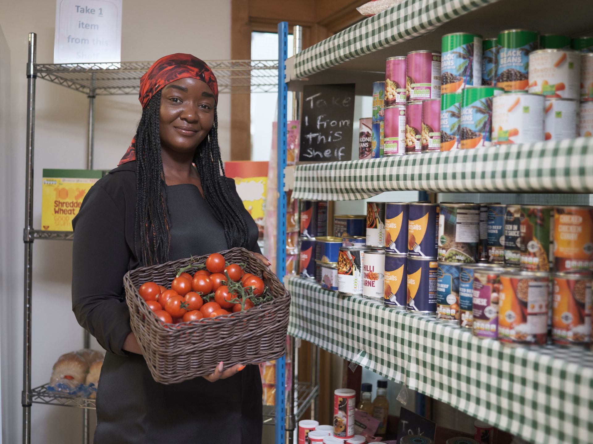 A woman is holding a basket of tomatoes in a pantry.