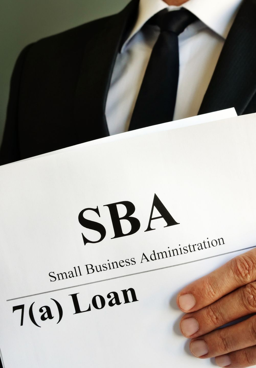 Man in a suit holding SBA 7(a) loan documents.