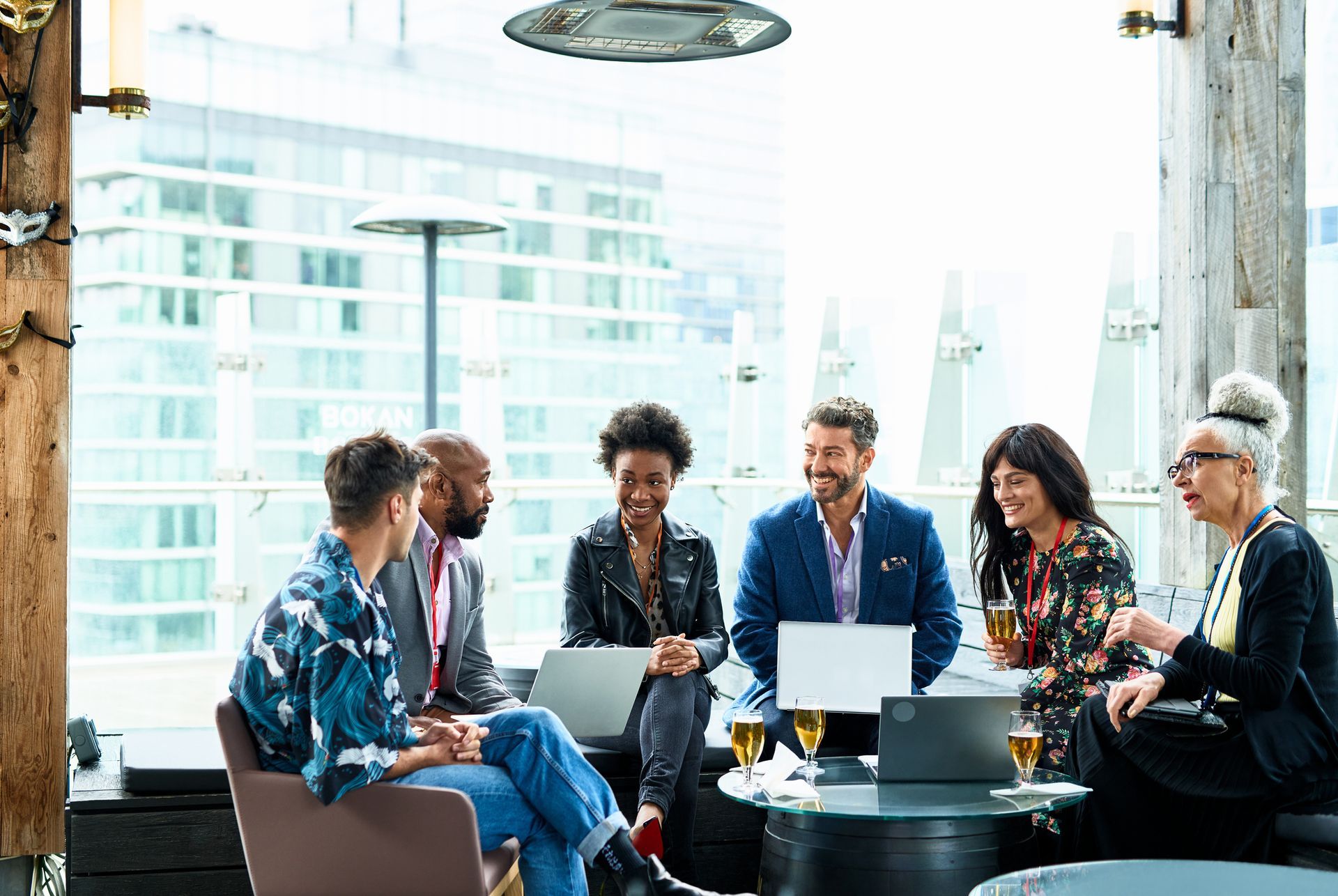 Group of diverse people in a modern office, laptops open, discussing around a table with city view.