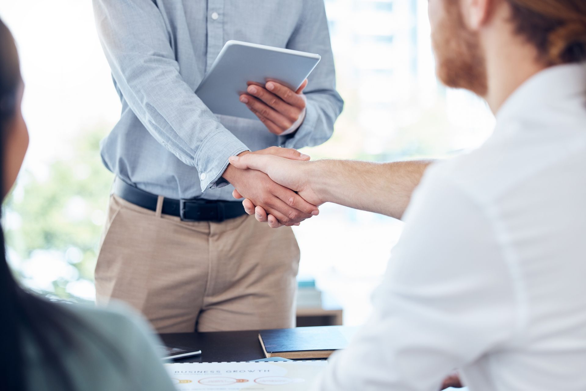 Business people shaking hands, deal closed. Office setting with a tablet held.