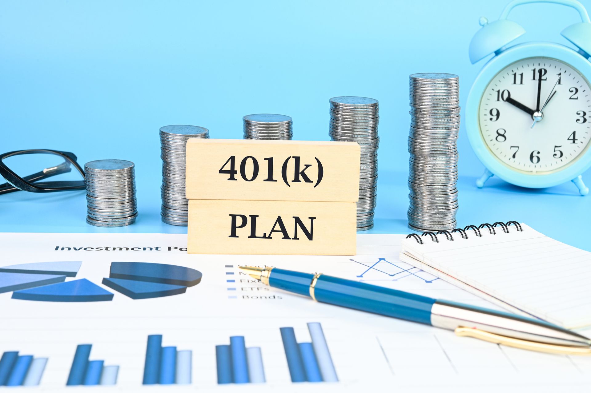 Stacks of coins, charts, pen, clock, and 401(k) PLAN on blue background.
