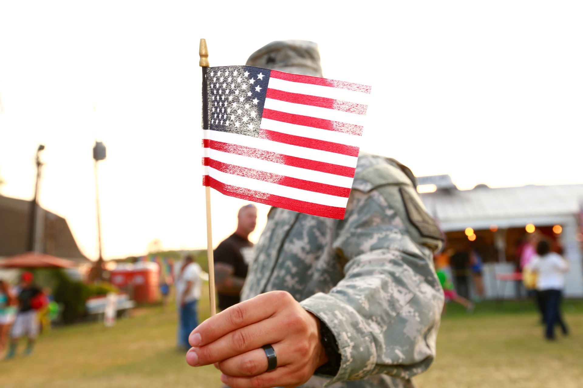 Soldier holding American flag at an outdoor gathering.