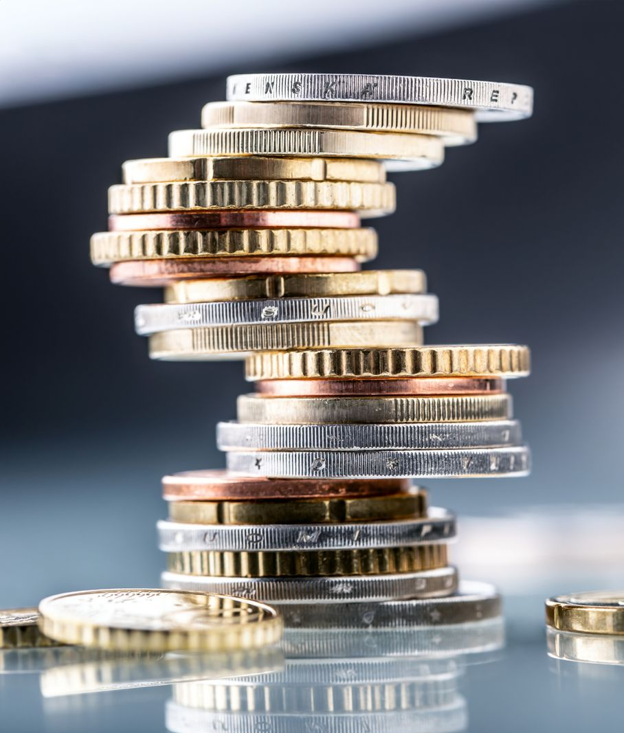 Stack of coins teetering precariously; scattered coins in the blurred background; reflective surface.