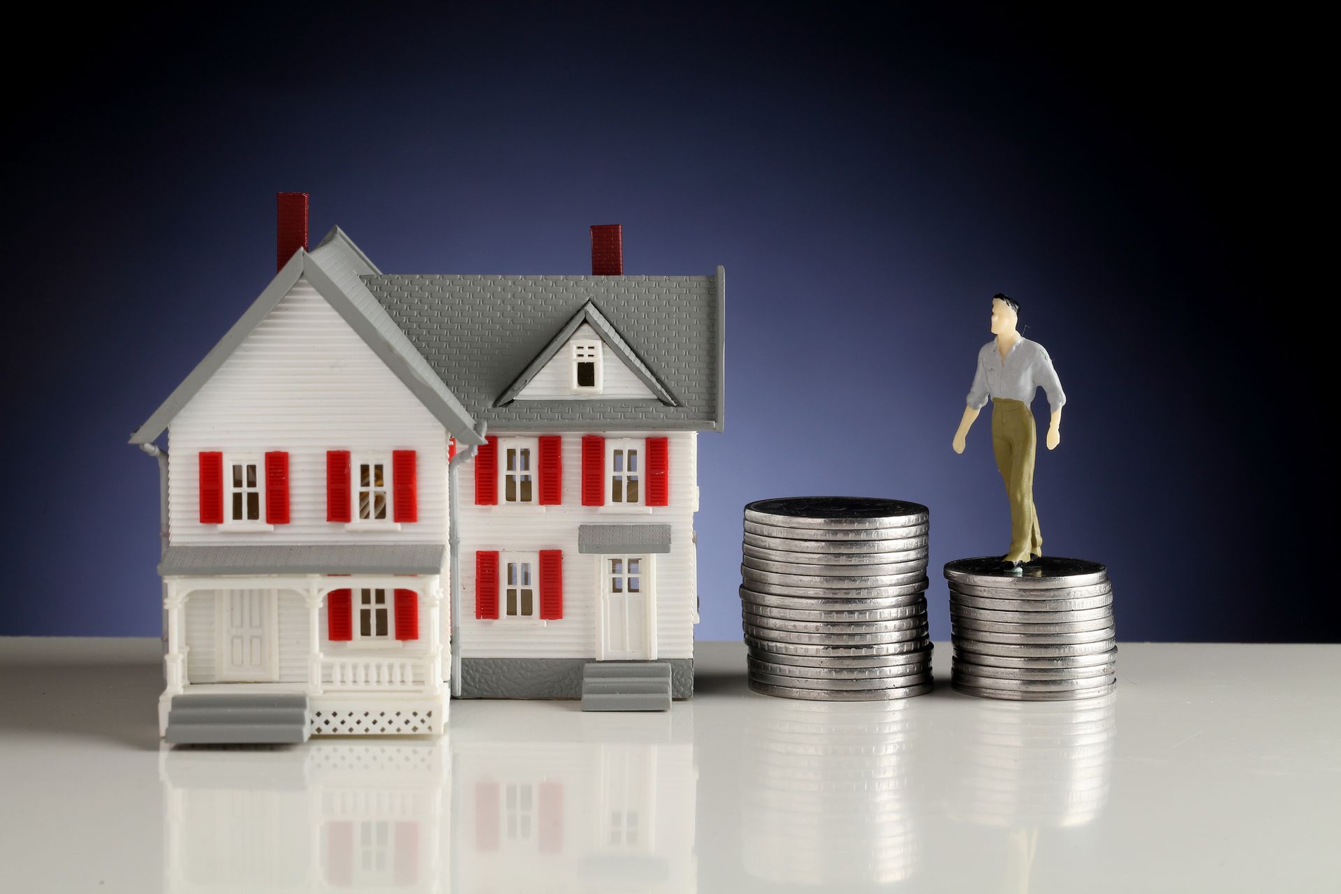 Model house next to stacks of coins with a tiny figurine standing on top, representing homeownership.