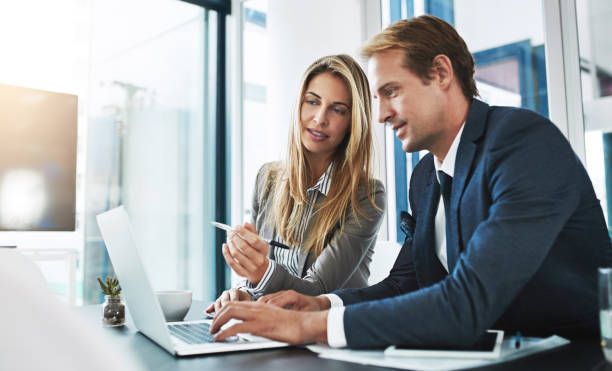 Woman and man in suits looking at laptop, discussing, pointing indoors.