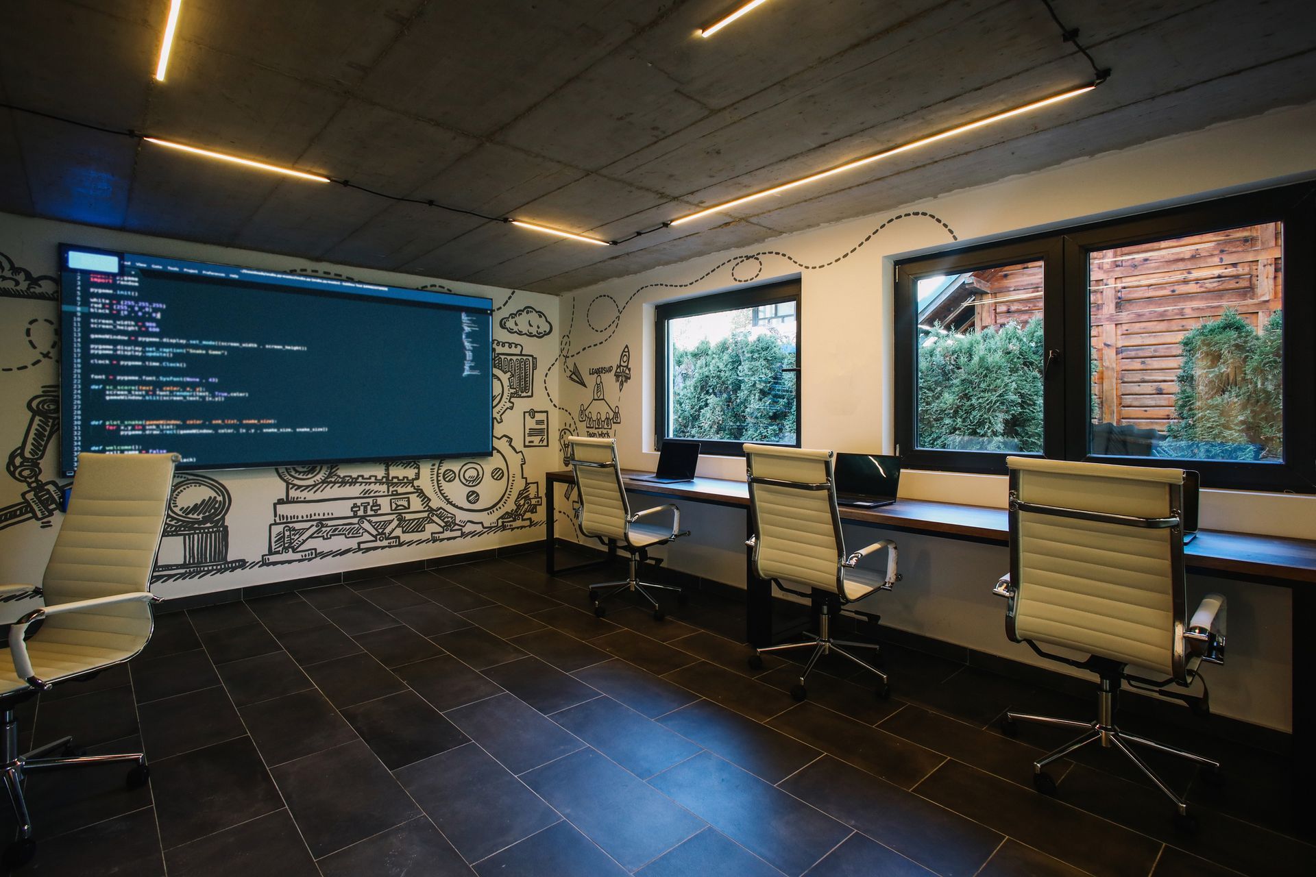 Office space with illustrated wall prints, desks, and a screen displaying code. Office space with illustrated wall prints, desks, and a screen displaying code.