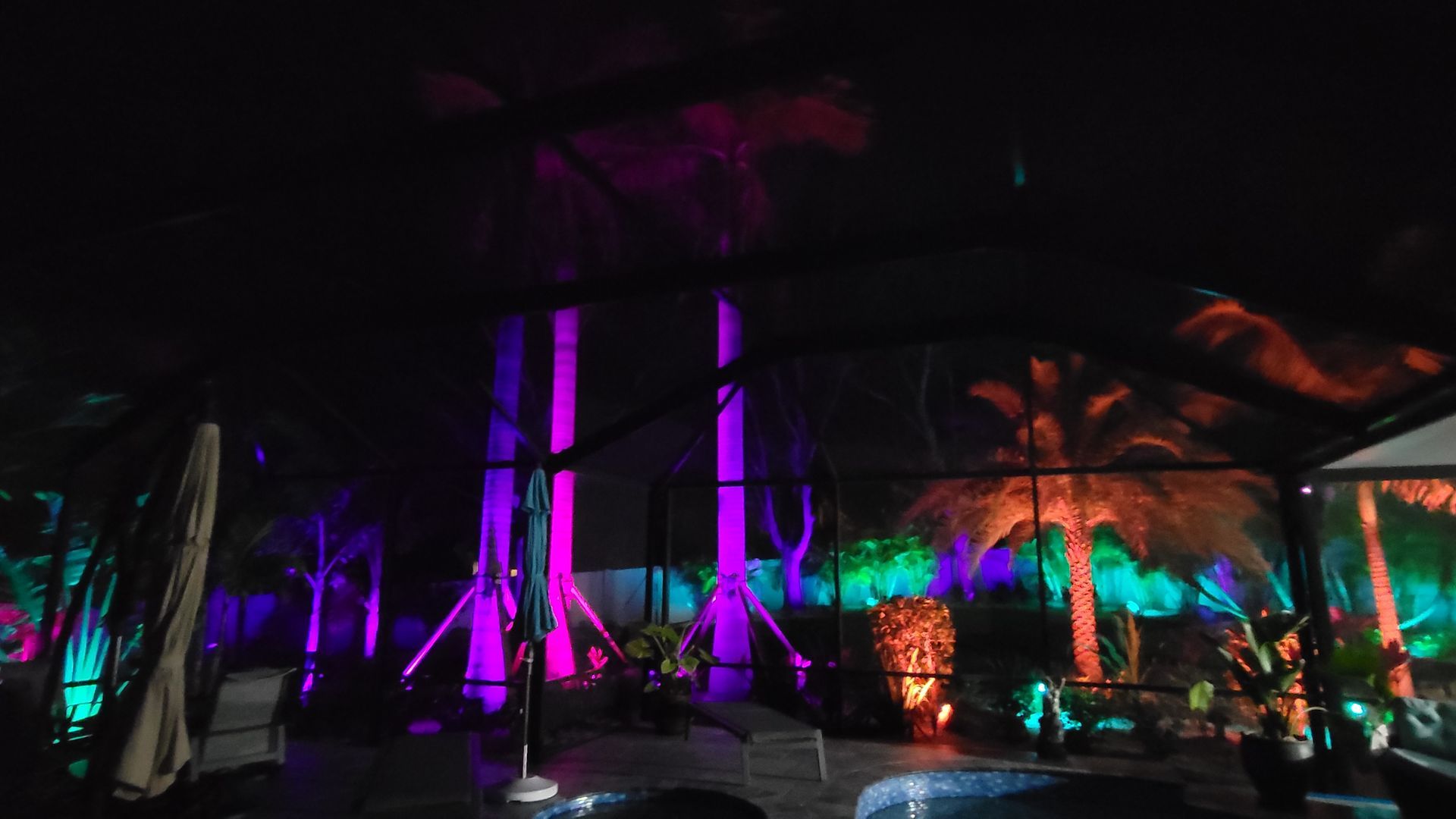 A swimming pool is lit up with purple and green lights at night.