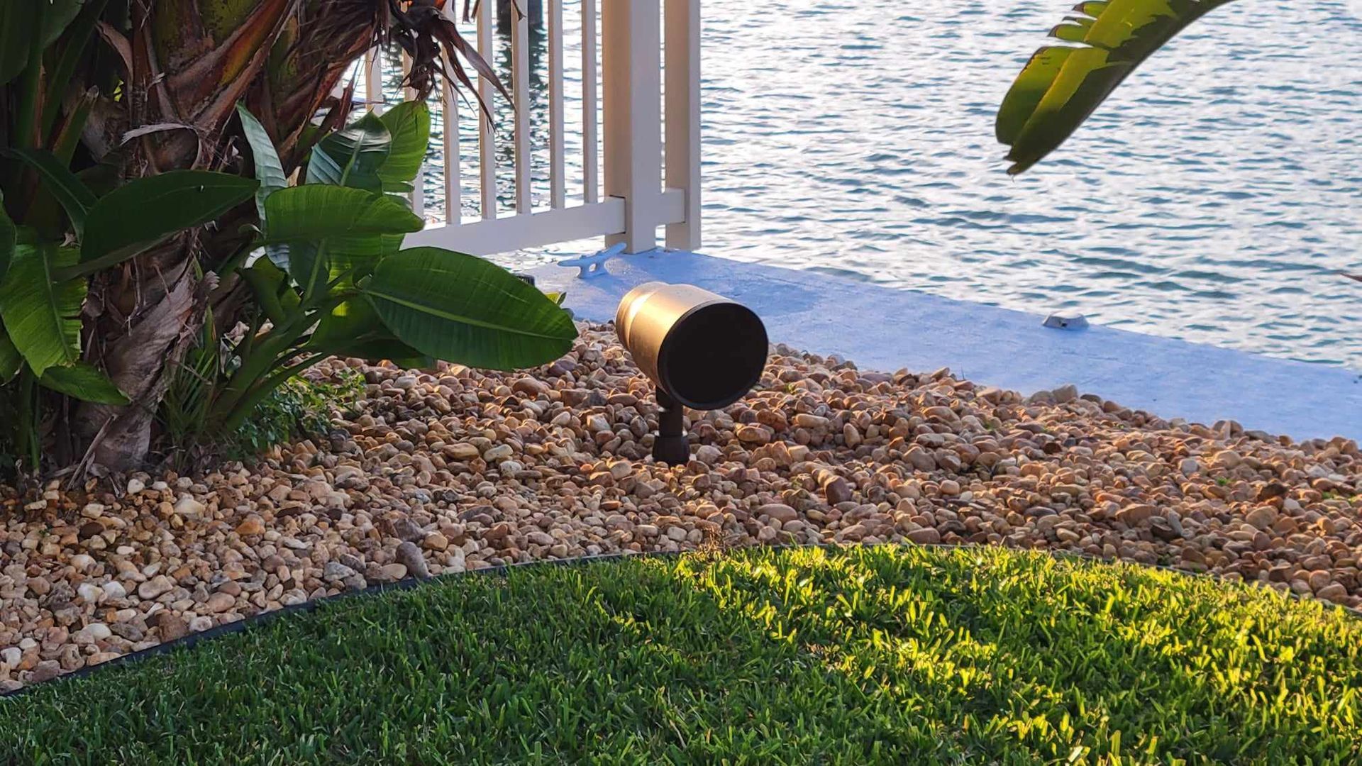 A lamp is sitting in the grass next to a body of water.