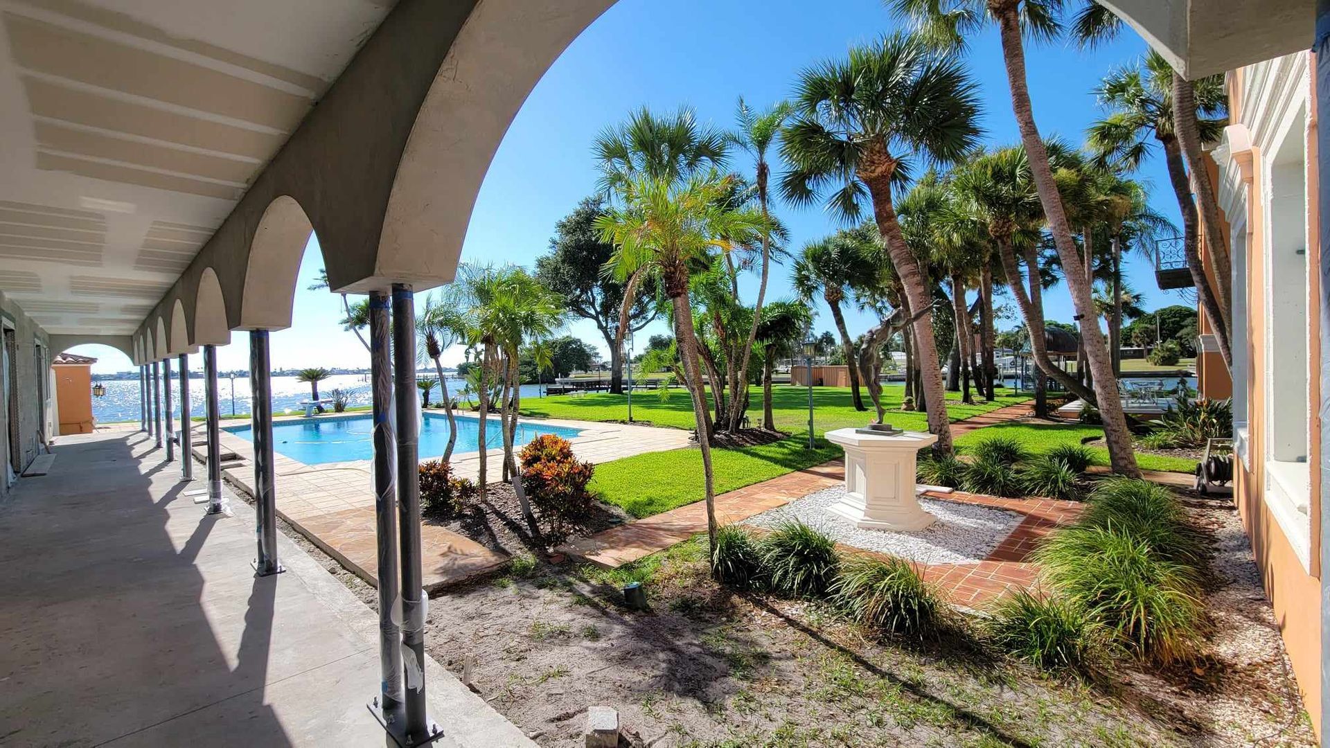 A long walkway with arches leading to a swimming pool surrounded by palm trees.