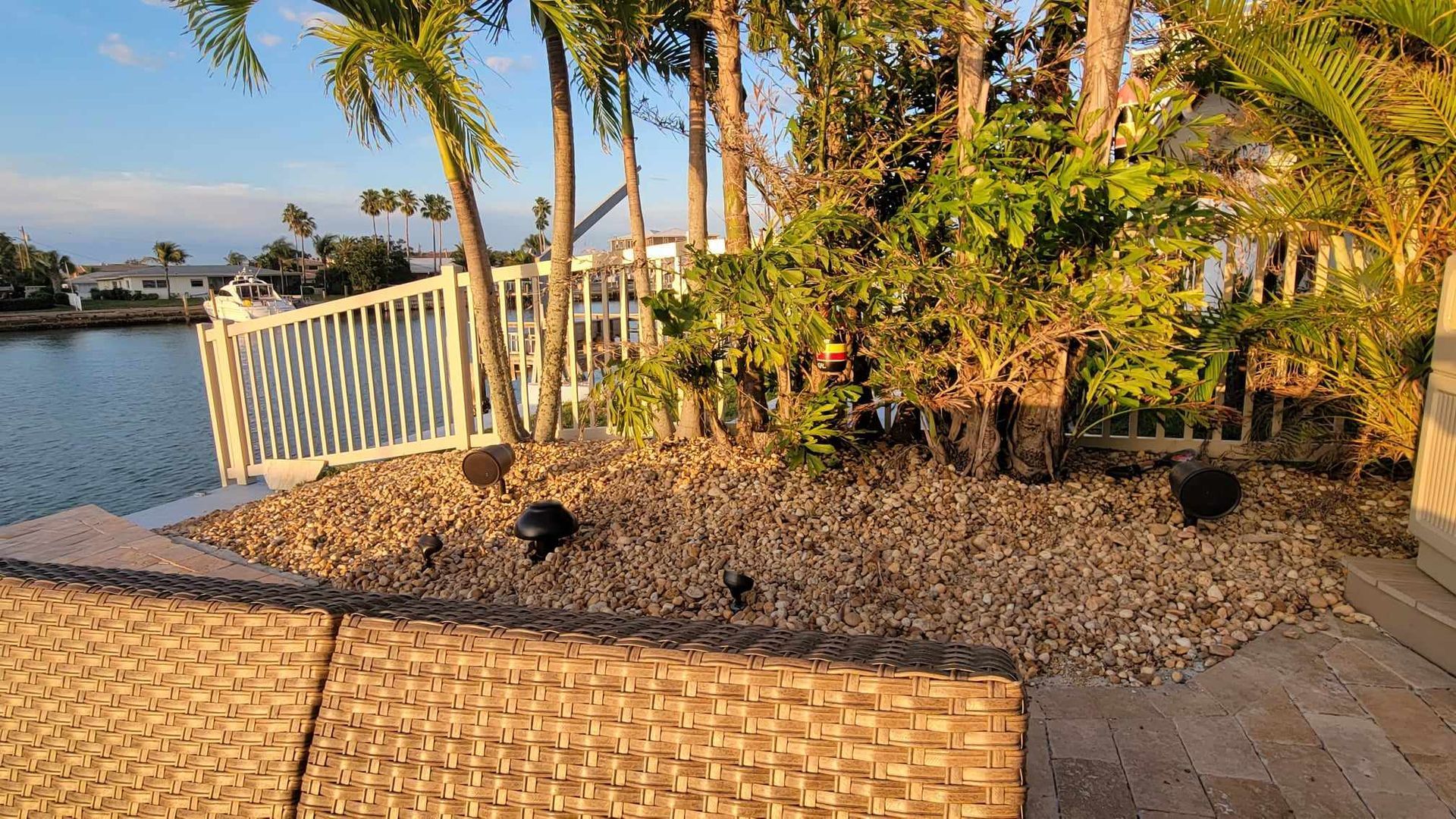 A patio with a wicker chair and a fence overlooking a body of water.