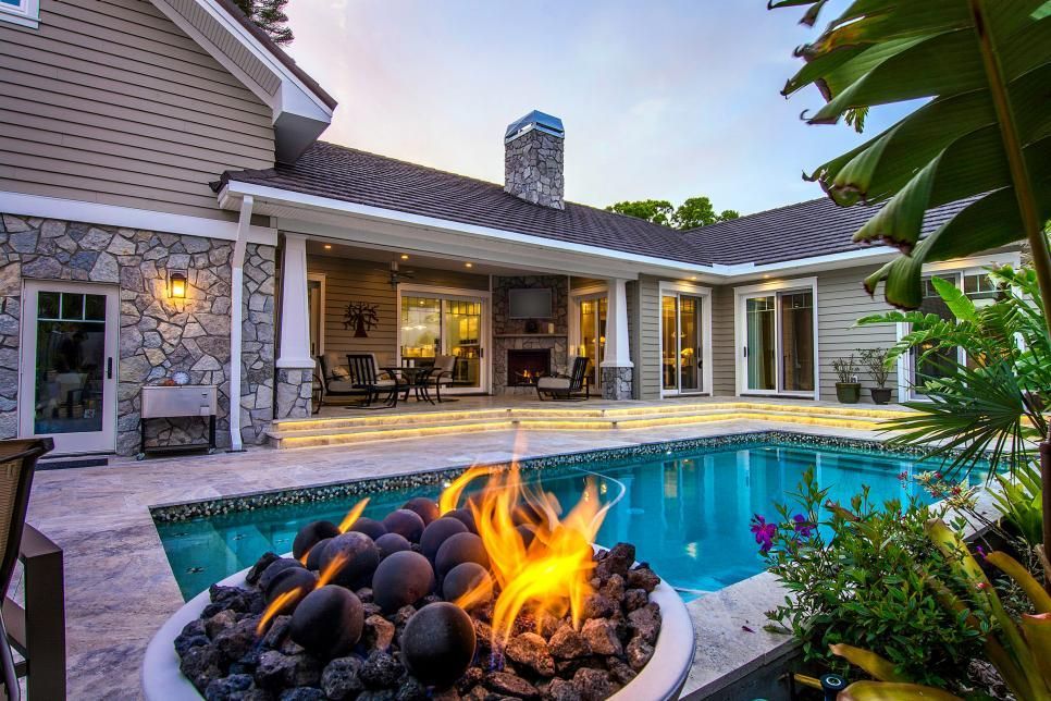 A fire pit is sitting next to a swimming pool in front of a house.