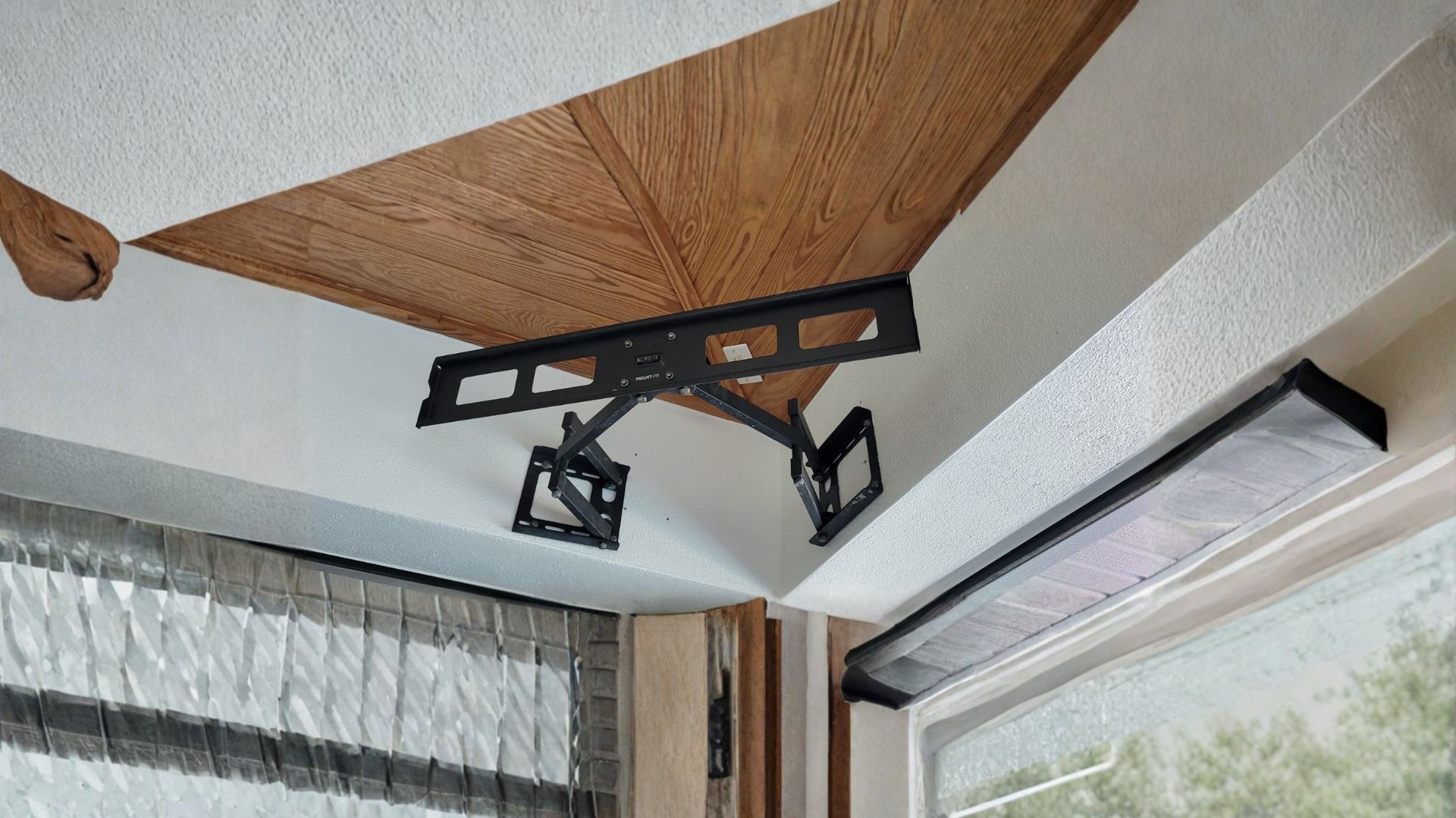 A ceiling-mounted swivel television bracket installed in the corner of a room next to a long rectangular light fixture.