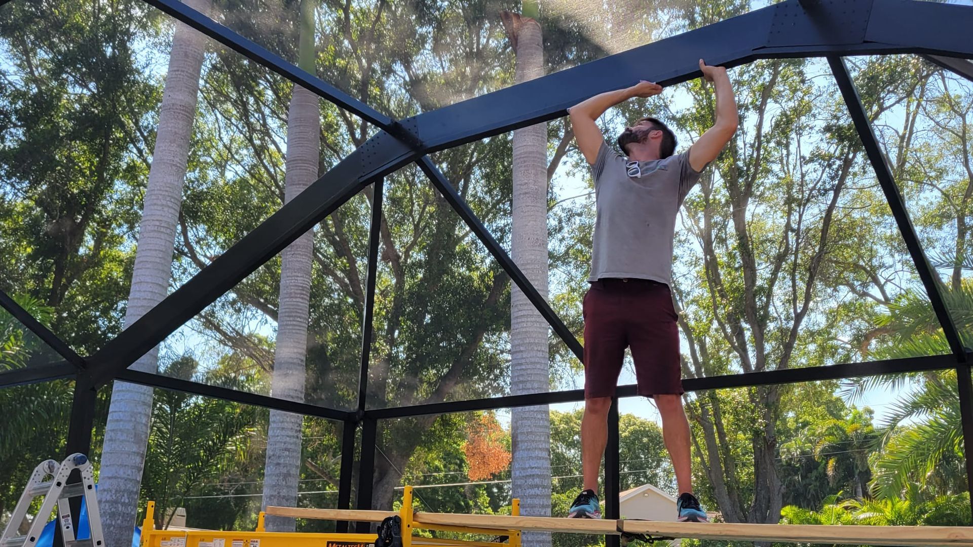 A man is standing on a scaffolding working on a screened in porch.