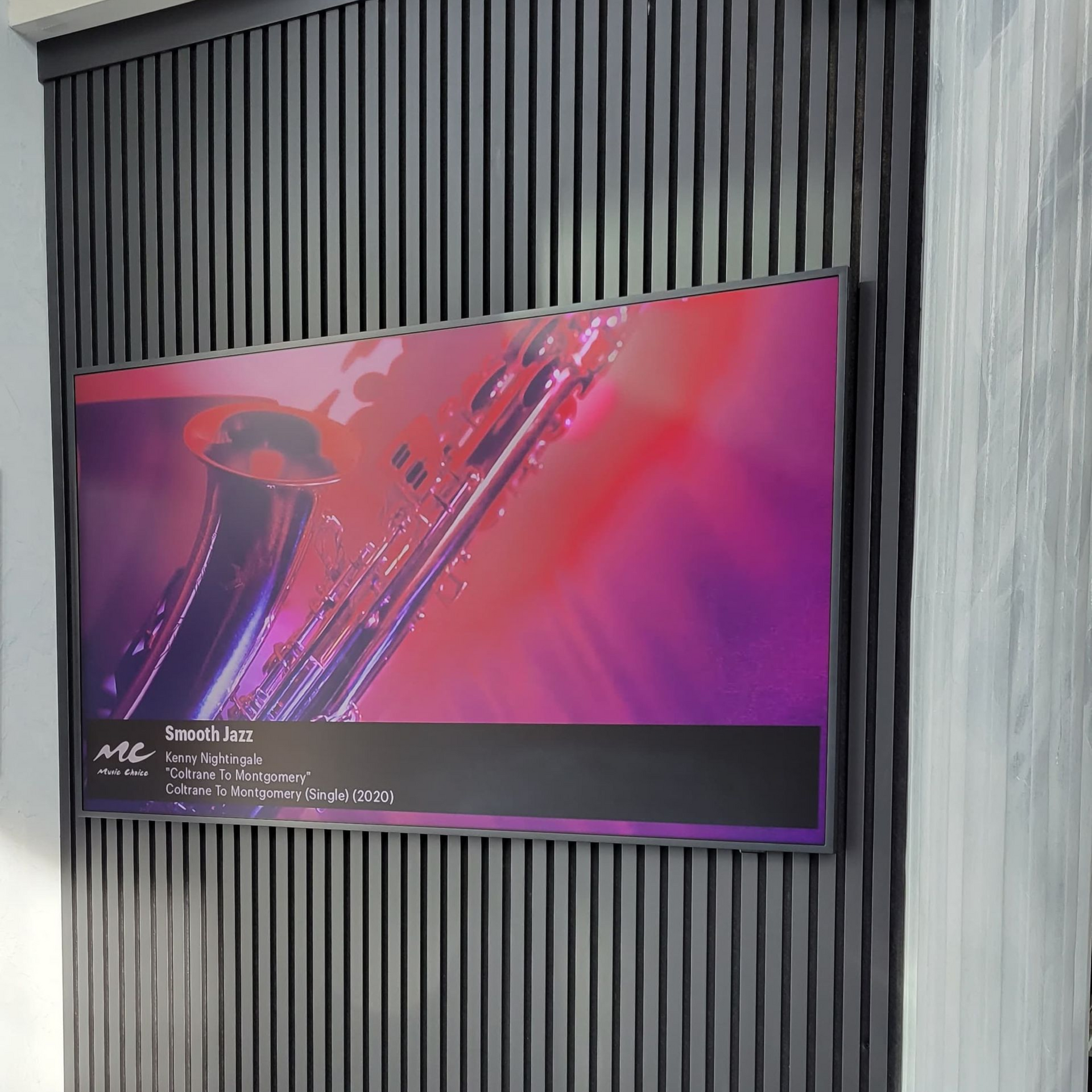 Television mounted on a textured, dark gray wall, displaying a saxophone graphic with purple and red hues.