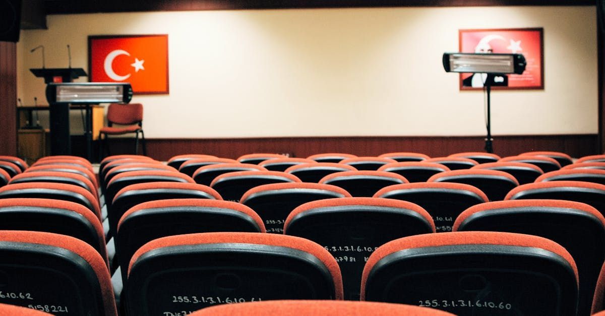 A row of empty seats in an auditorium with a flag on the wall.