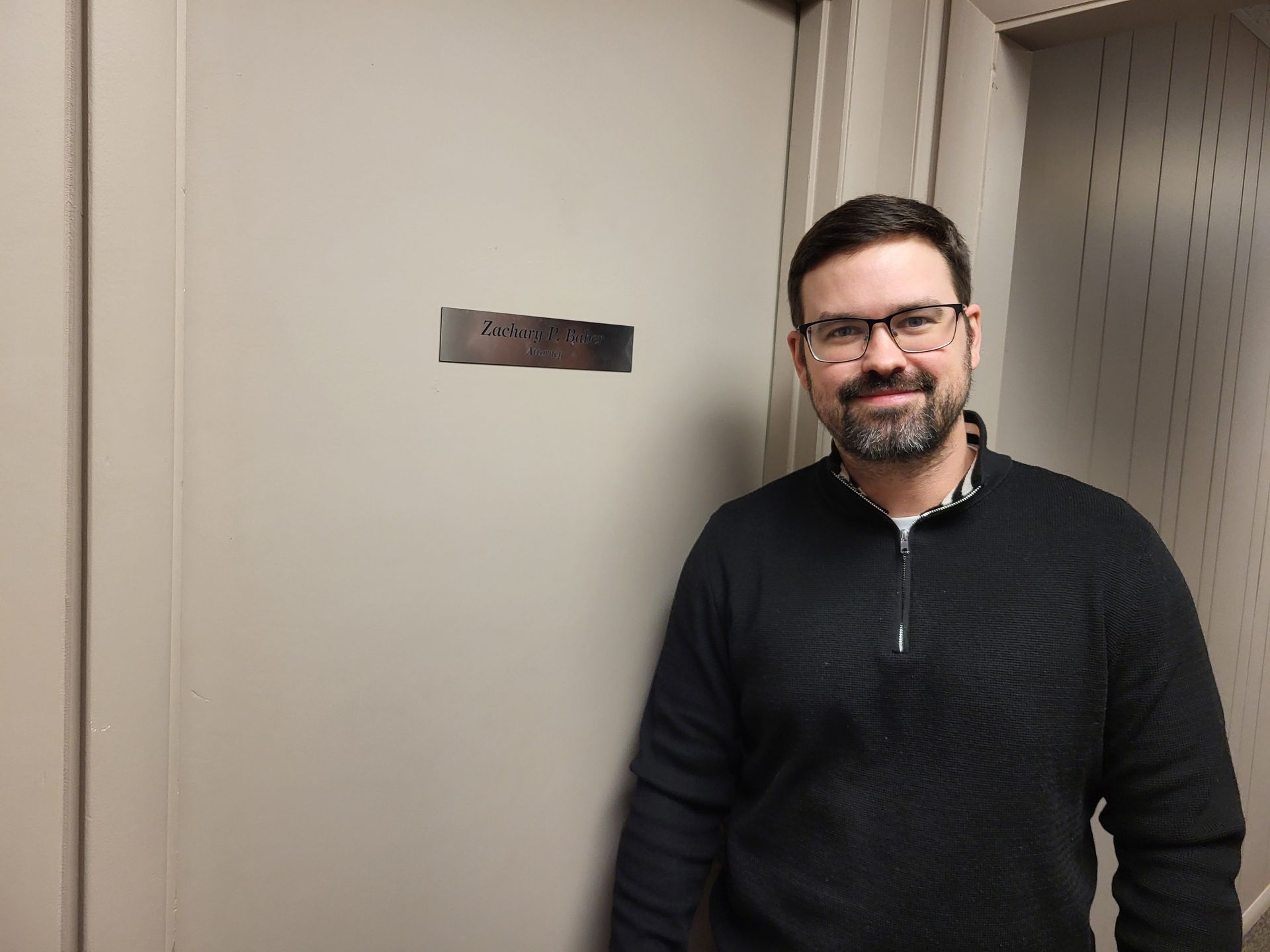 Zach Baber, attorney near Fort Wayne, standing beside his inside office door.