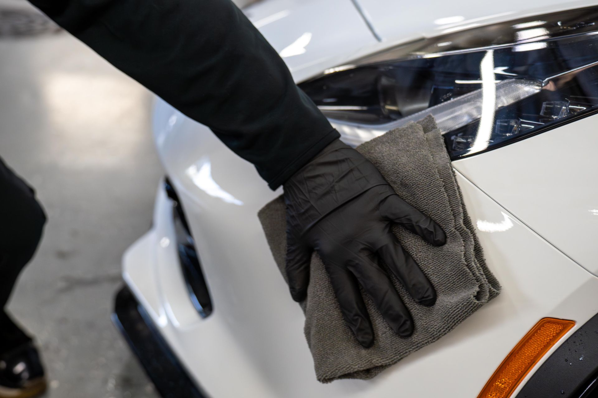A person wearing black gloves is cleaning a white car with a towel.