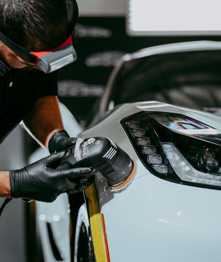A man is polishing the headlight of a white car.