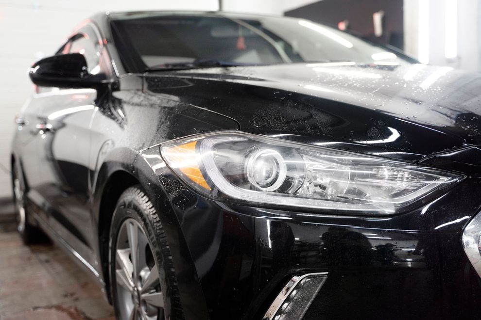 A black car is parked in a garage next to a wall.
