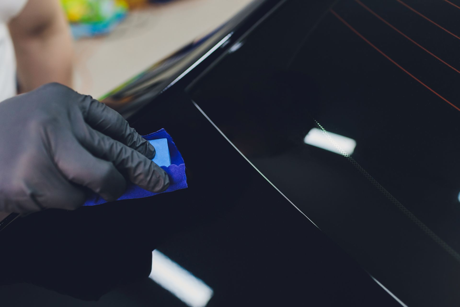 A person wearing black gloves is applying ceramic coating to a black car.