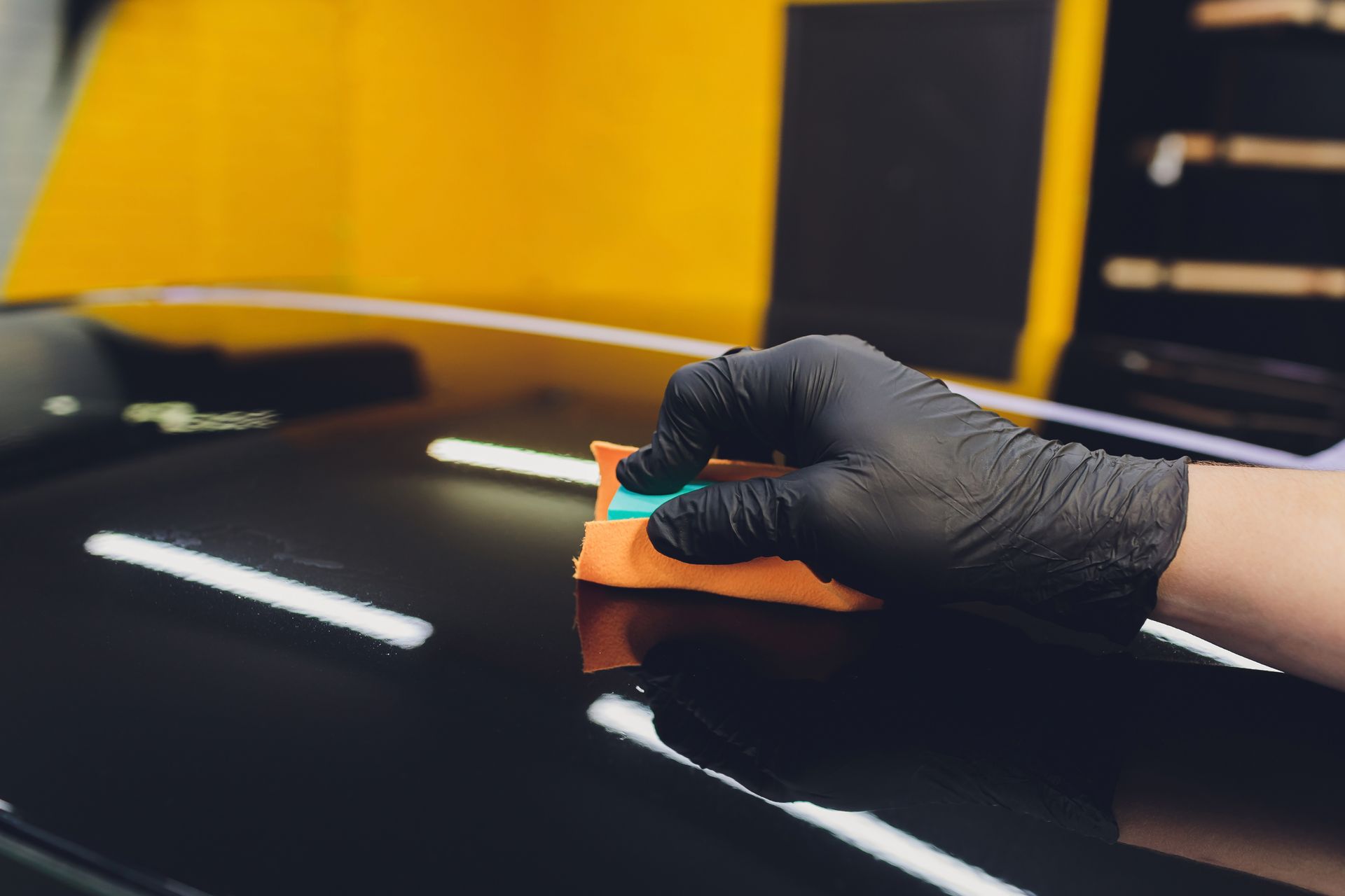 A person wearing black gloves is polishing the hood of a car.