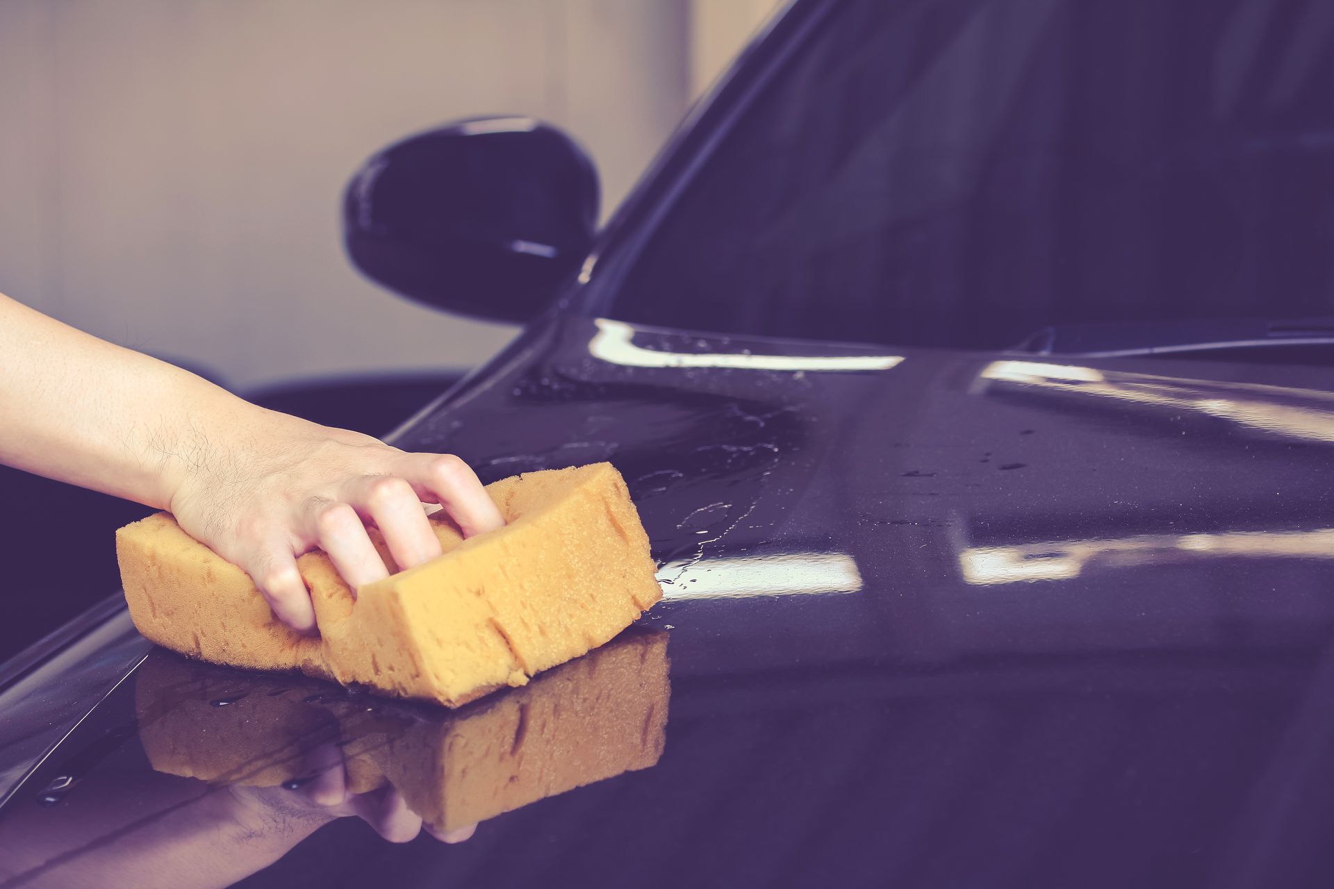 A person is cleaning the hood of a car with a sponge.