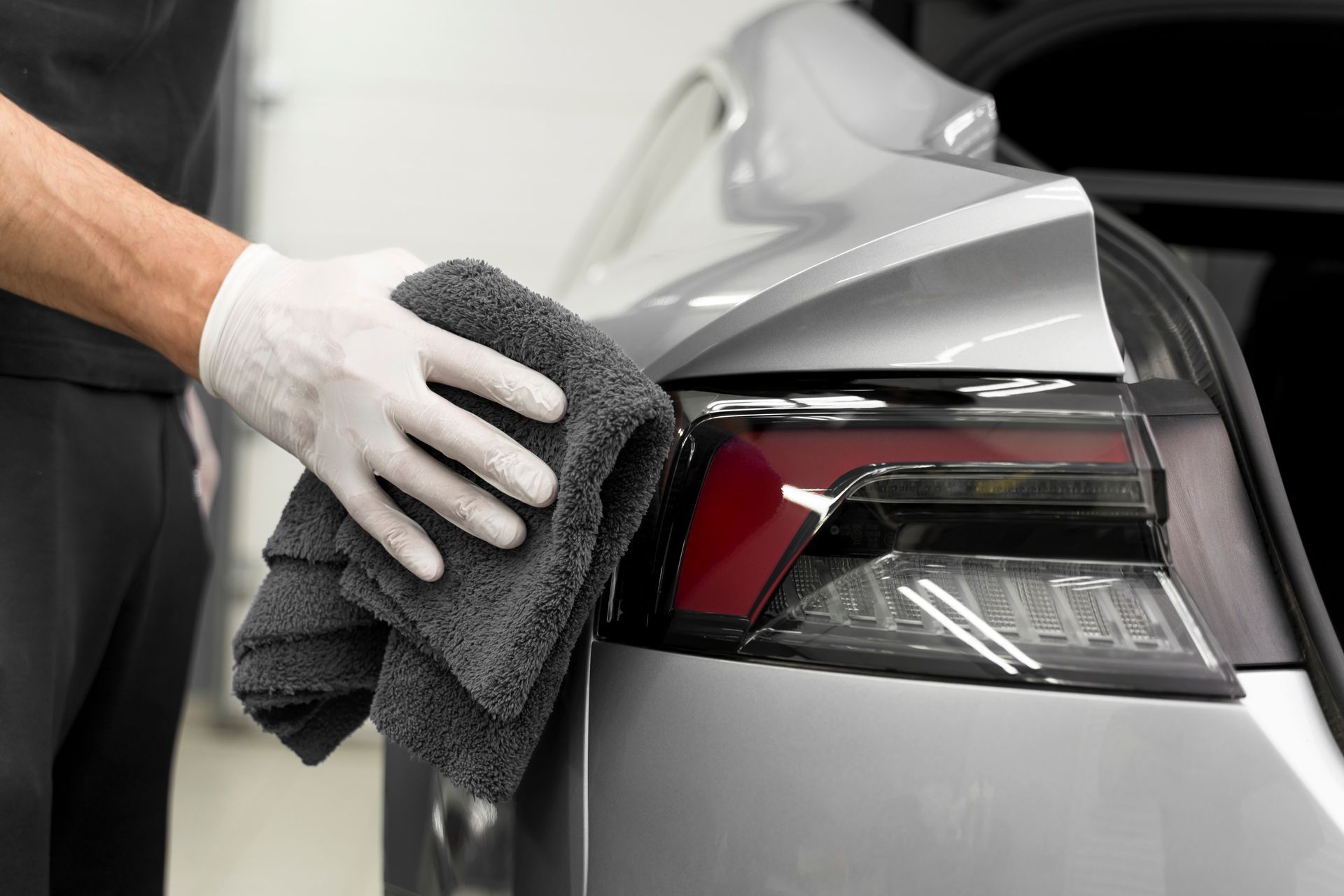 A person is cleaning a car with a towel and gloves.