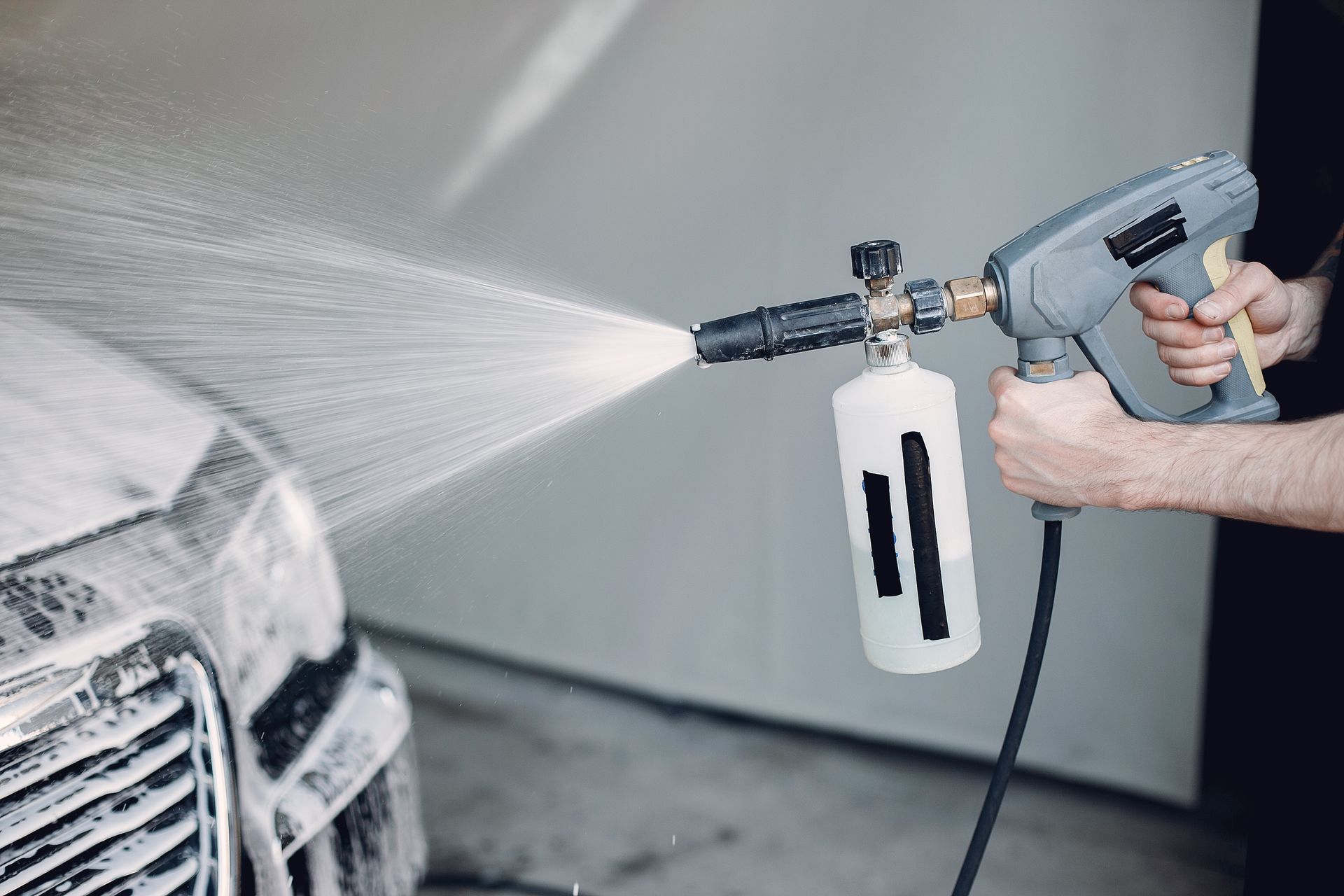 A man is washing a car with a high pressure washer.